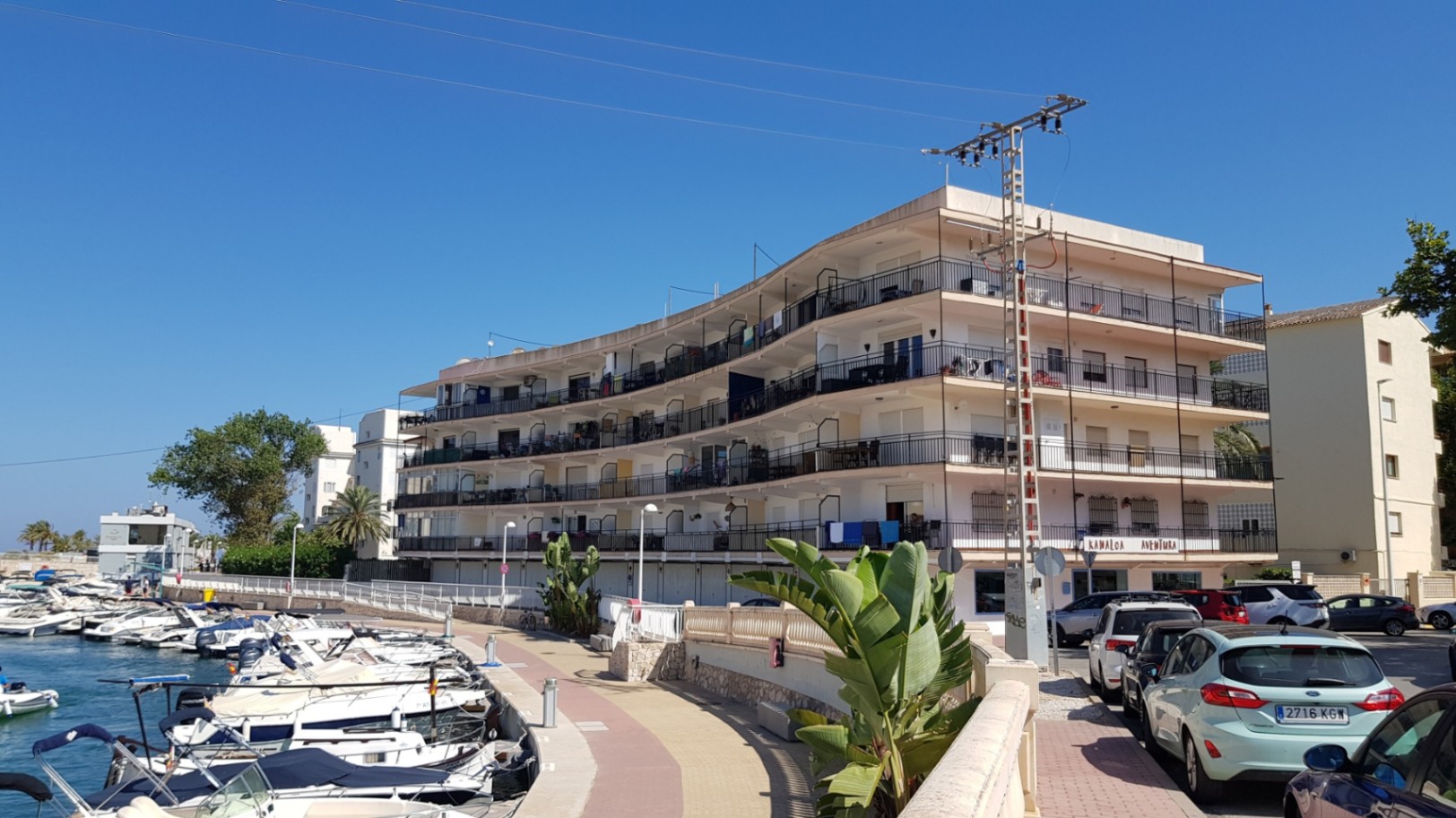 Vue extérieure du bâtiment avec balcons incurvés et garde-corps en fer, situé face au canal de la marina avec ses bateaux de plaisance à Jávea.