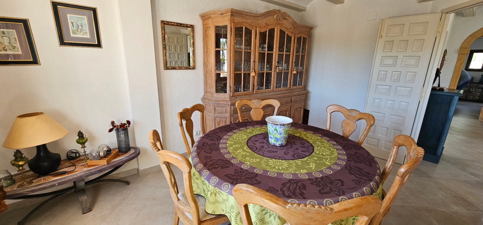 Coin repas rustique avec table circulaire, chaises en bois sculpté et un grand buffet classique. La pièce dispose d'un sol en céramique et d'une décoration traditionnelle.
