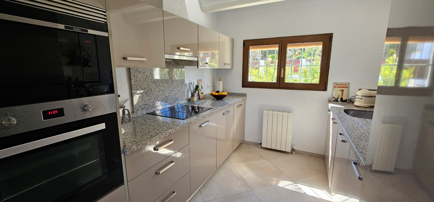 Cuisine indépendante avec meubles laqués, plan de travail en granit et électroménager encastré. Une fenêtre avec cadre en bois offre une belle luminosité naturelle.