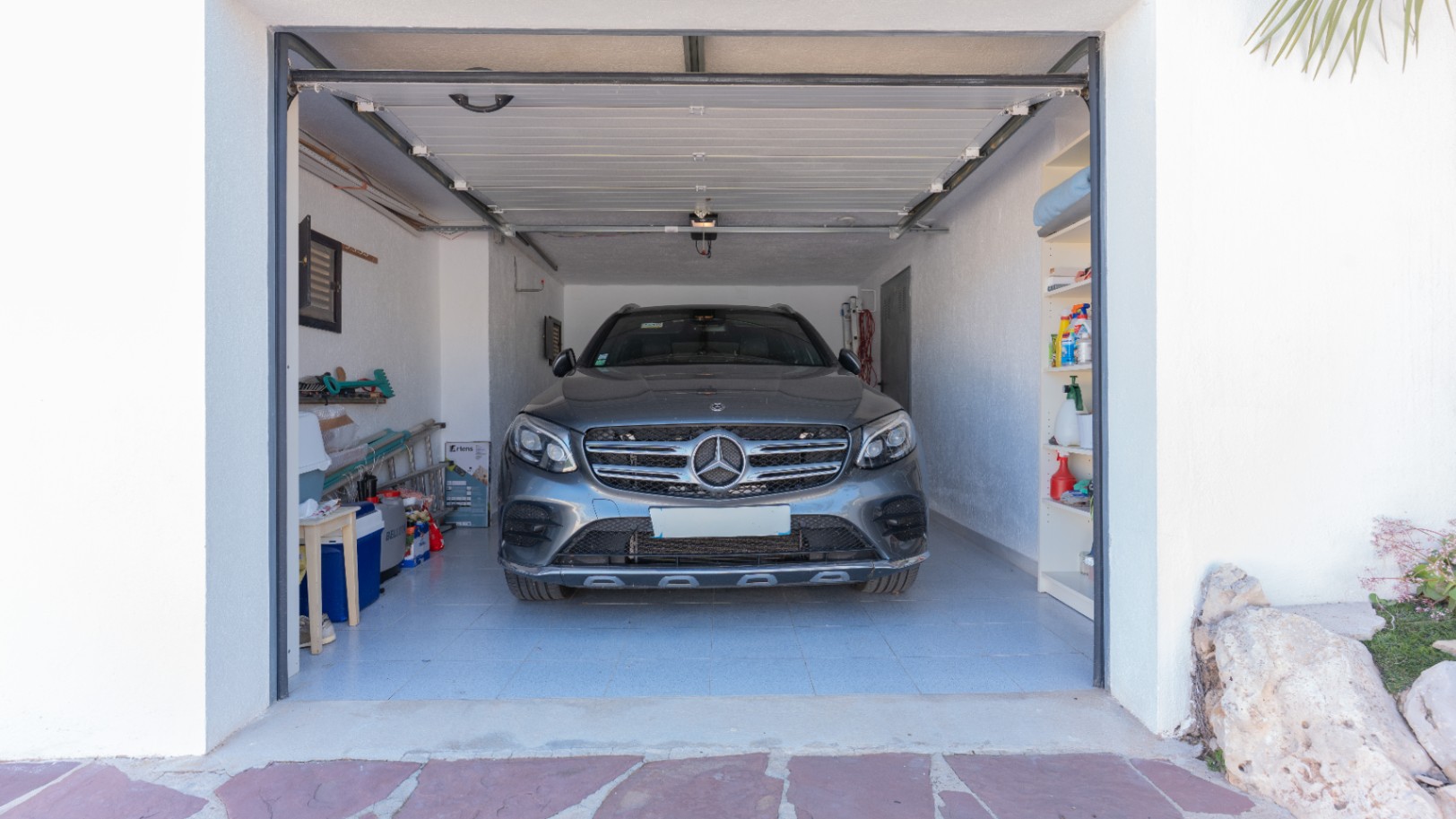 Garage privé avec sol carrelé, étagères intégrées et porte sectionnelle automatique, offrant un espace de rangement généreux et une protection pour les véhicules.