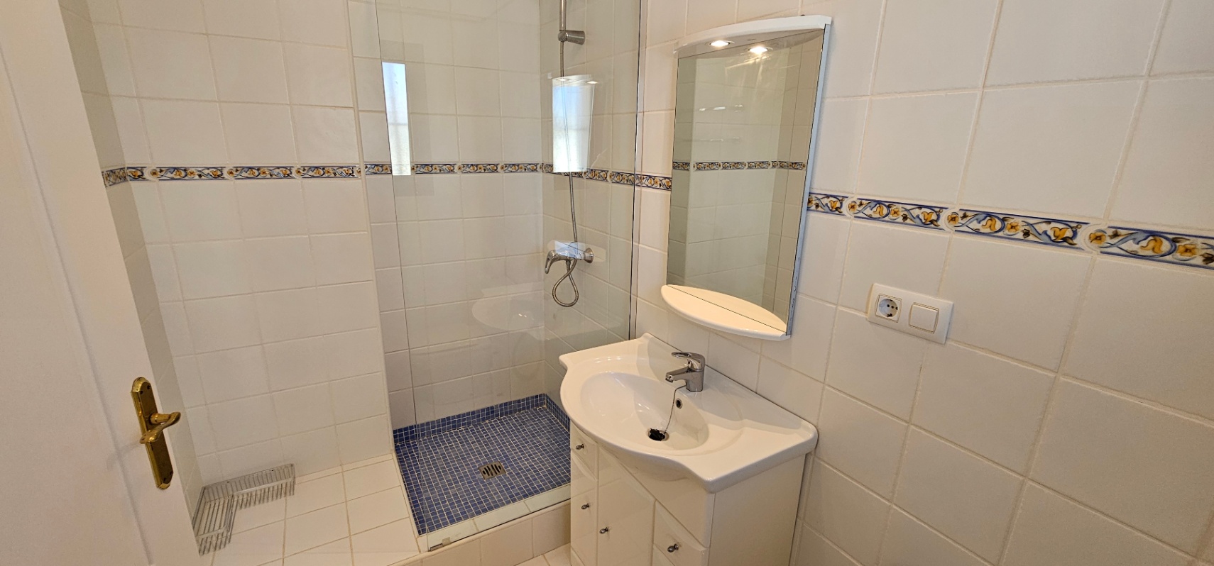 Salle de bain fonctionnelle avec douche à l'italienne en mosaïque bleue, paroi vitrée, meuble vasque blanc et miroir éclairé.