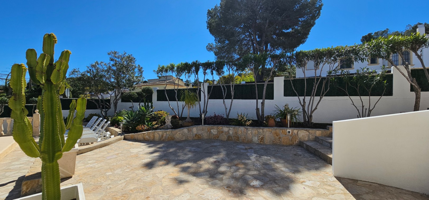 Terrasse extérieure en pierre naturelle avec murets de soutènement. Le jardin paysager intègre des cactus et une végétation méditerranéenne variée.