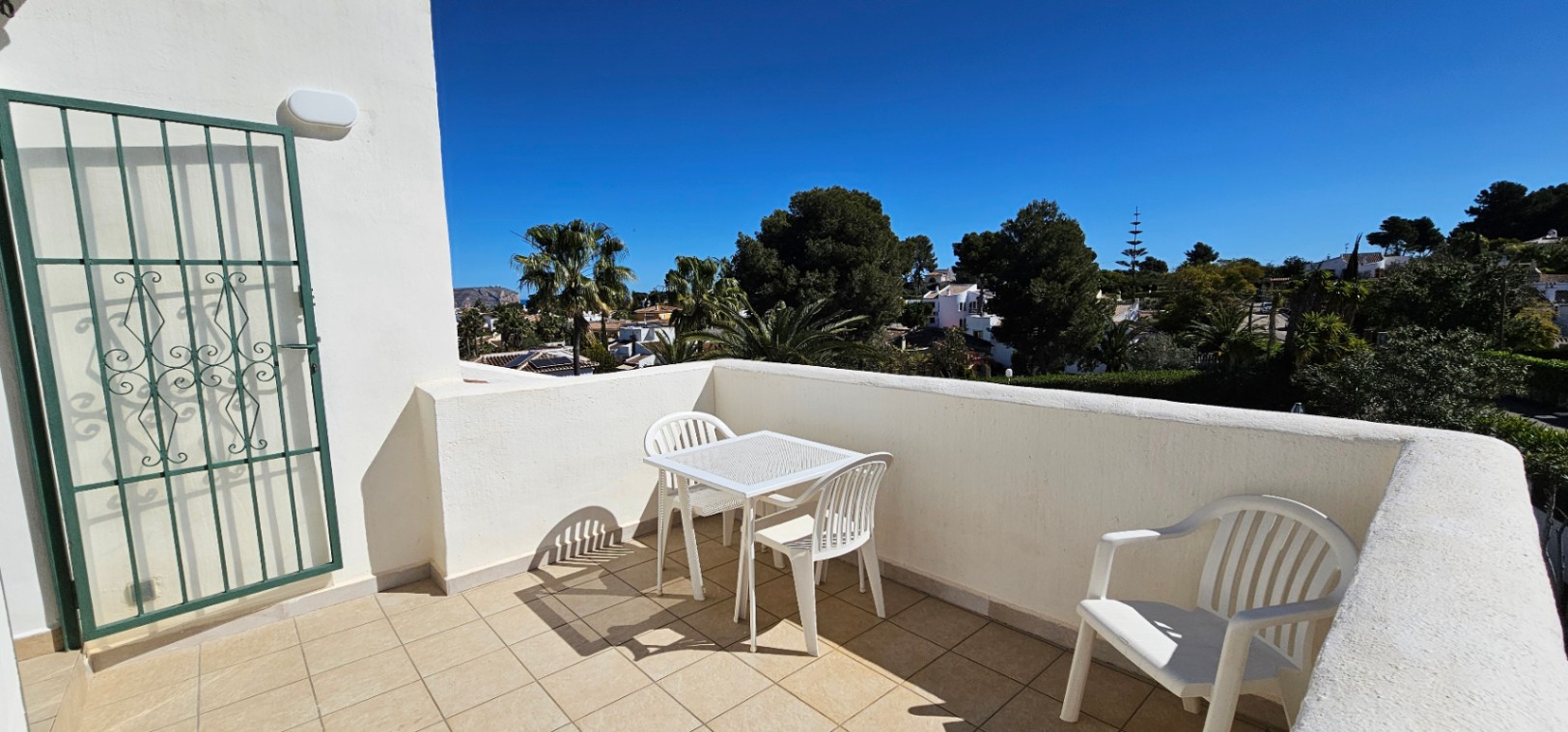 Terrasse ouverte à l'étage avec carrelage clair, mobilier de jardin blanc et vue sur le quartier résidentiel arboré de Pinosol.