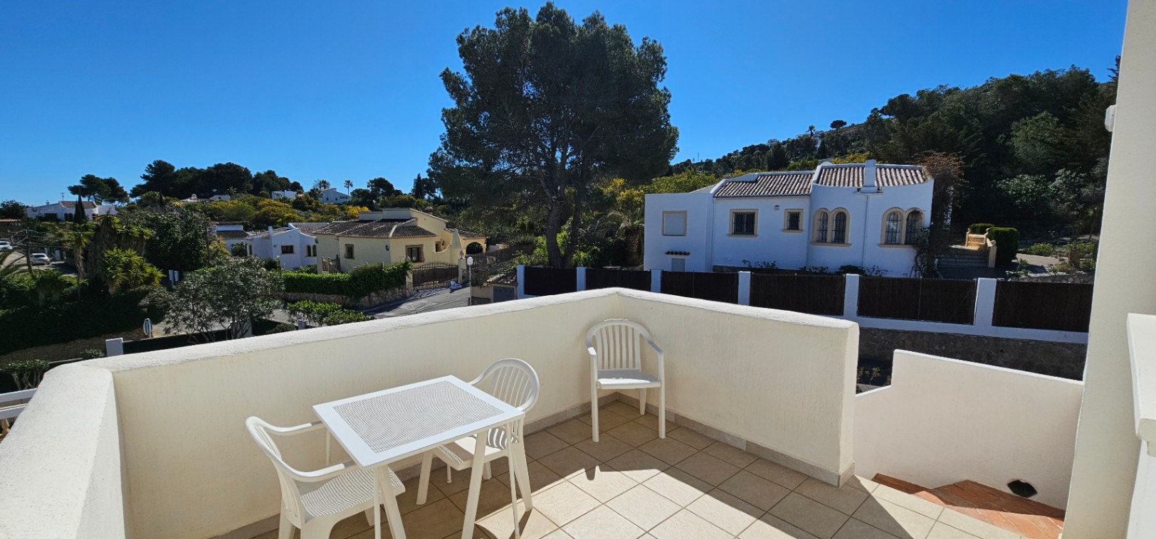 Terrasse ouverte à l'étage avec sol en grès et mobilier d'extérieur, offrant une vue dégagée sur le quartier résidentiel de Pinosol et les collines.