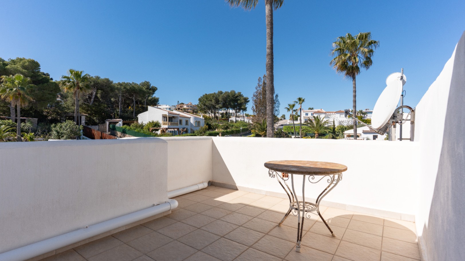 Terrasse supérieure avec sol en carrelage, table d'appoint en fer forgé et antenne satellite, offrant une vue dégagée sur le quartier de Pinosol.