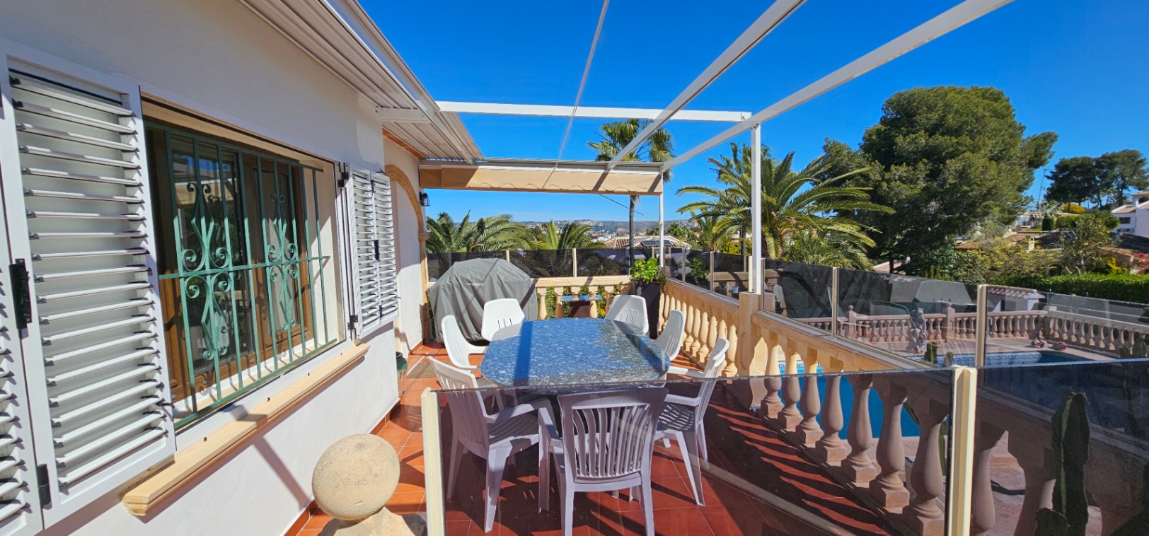Terrasse surélevée avec sol en terre cuite, table en granit et garde-corps en verre. Elle offre une vue sur la piscine et le paysage méditerranéen environnant.