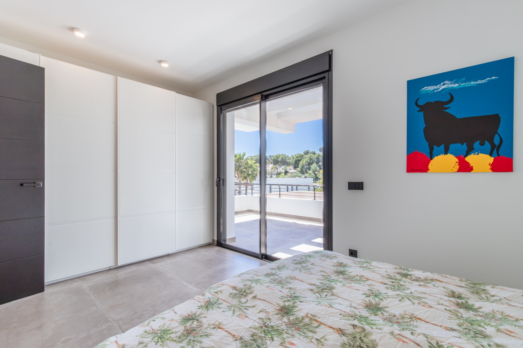Chambre avec placards intégrés blancs et accès direct à une terrasse privée via une grande baie vitrée, complétée par un sol en grès cérame.