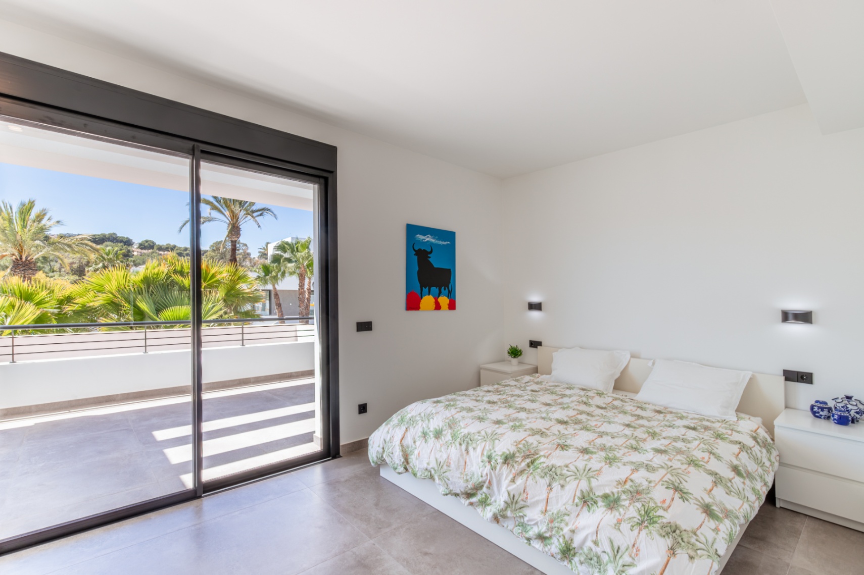 Chambre lumineuse avec accès direct à une terrasse privée par de grandes baies vitrées coulissantes. Sol en grès gris et éclairage mural intégré.