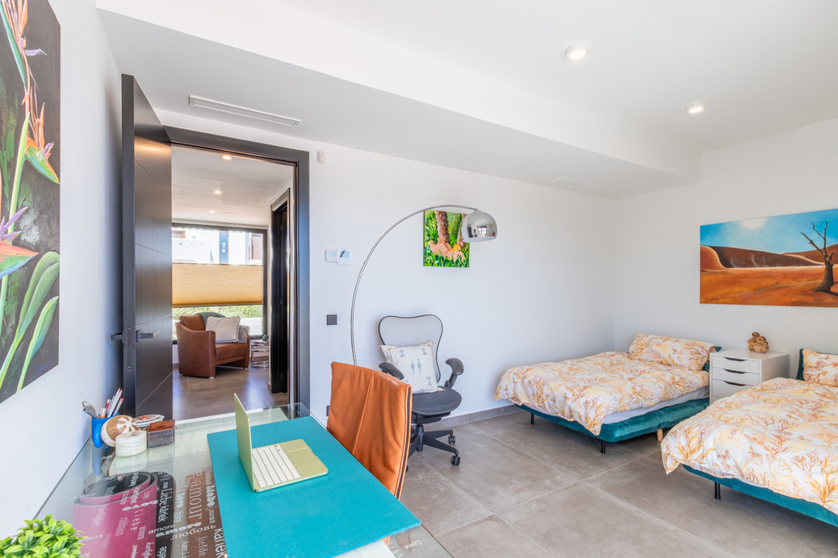 Chambre lumineuse avec lits jumeaux, coin bureau intégré et sol en grès cérame. L'espace dispose d'un éclairage encastré et d'une vue sur le dégagement avec fauteuil en cuir.