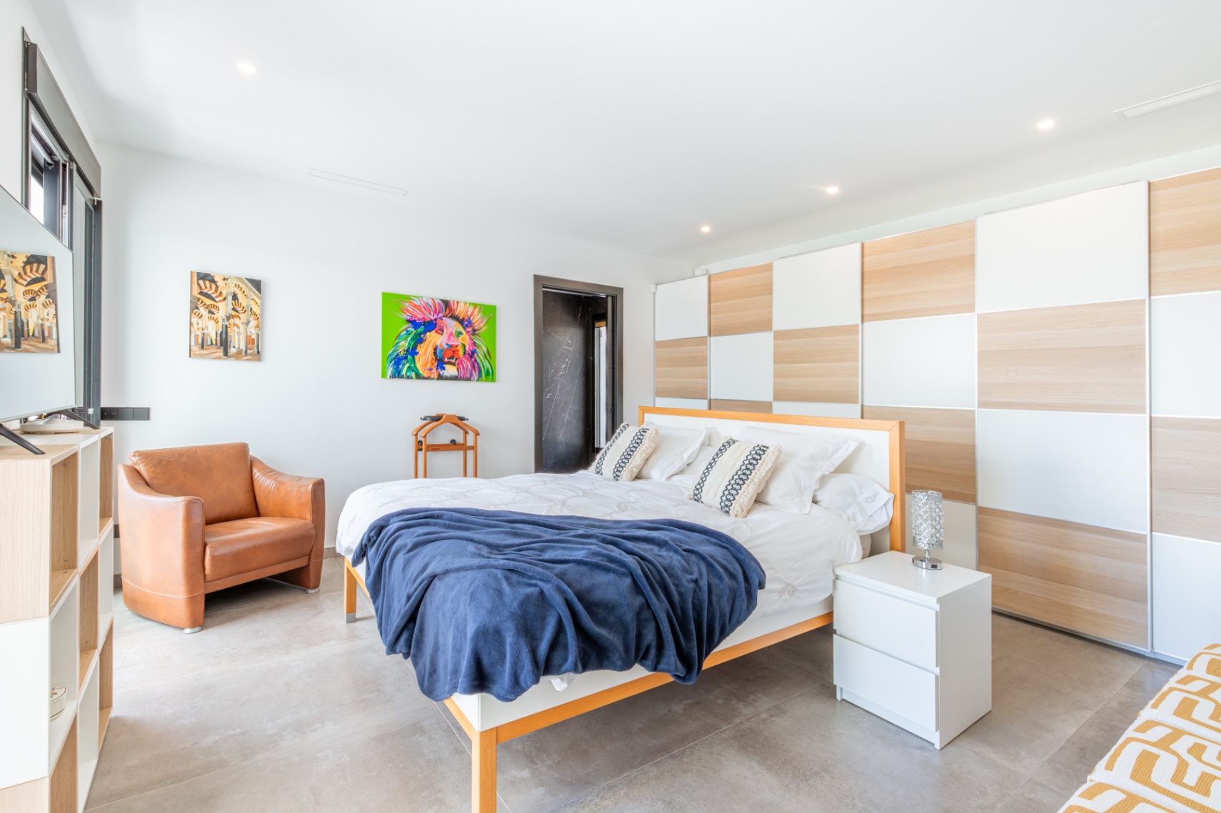 Chambre lumineuse dotée d'un grand placard intégré au motif damier bois et blanc, d'un sol en grès gris et d'un fauteuil en cuir élégant.