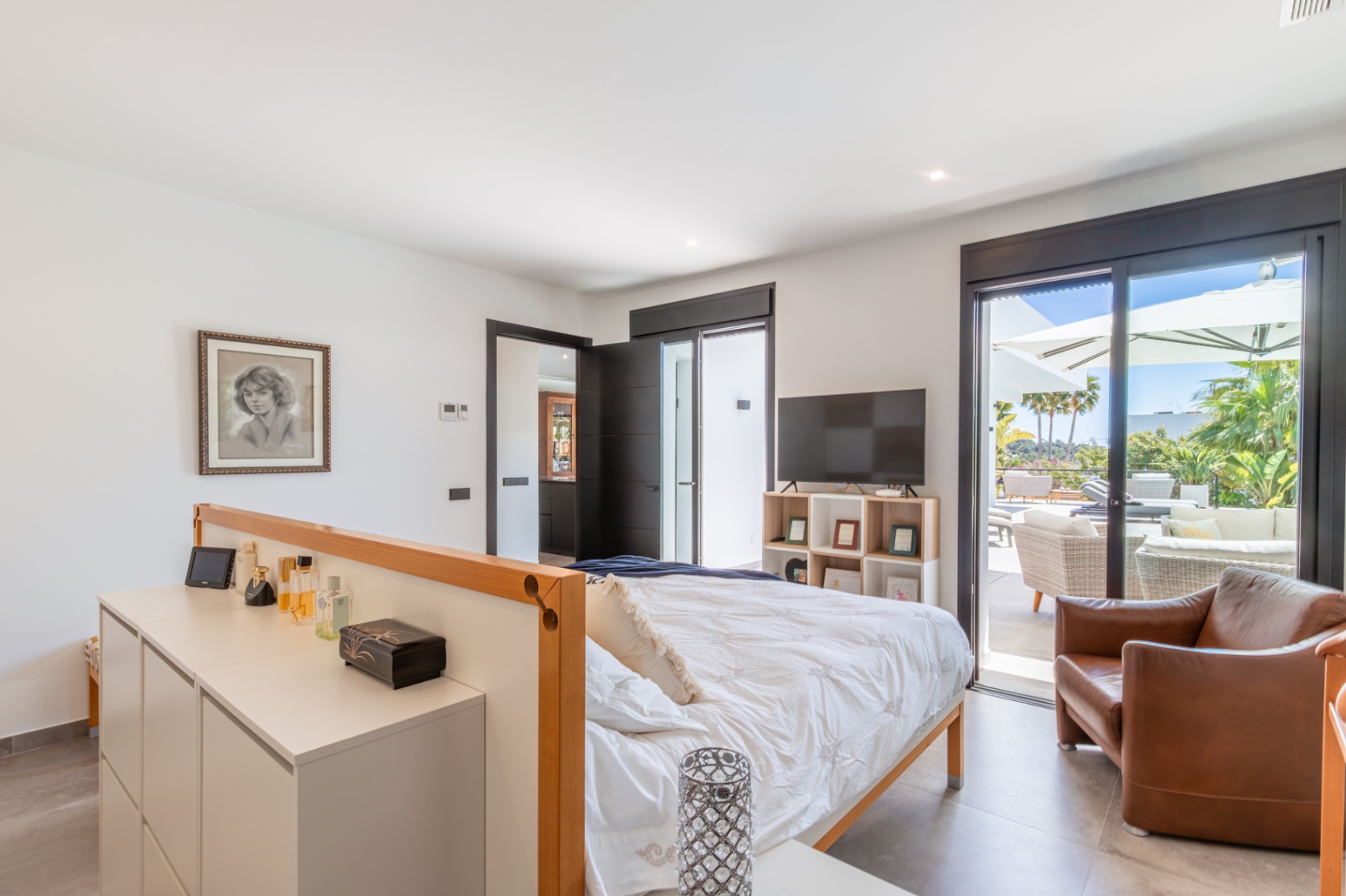 Chambre principale lumineuse avec accès direct à la terrasse, menuiseries noires élégantes et un agencement fluide incluant un coin salon privé.