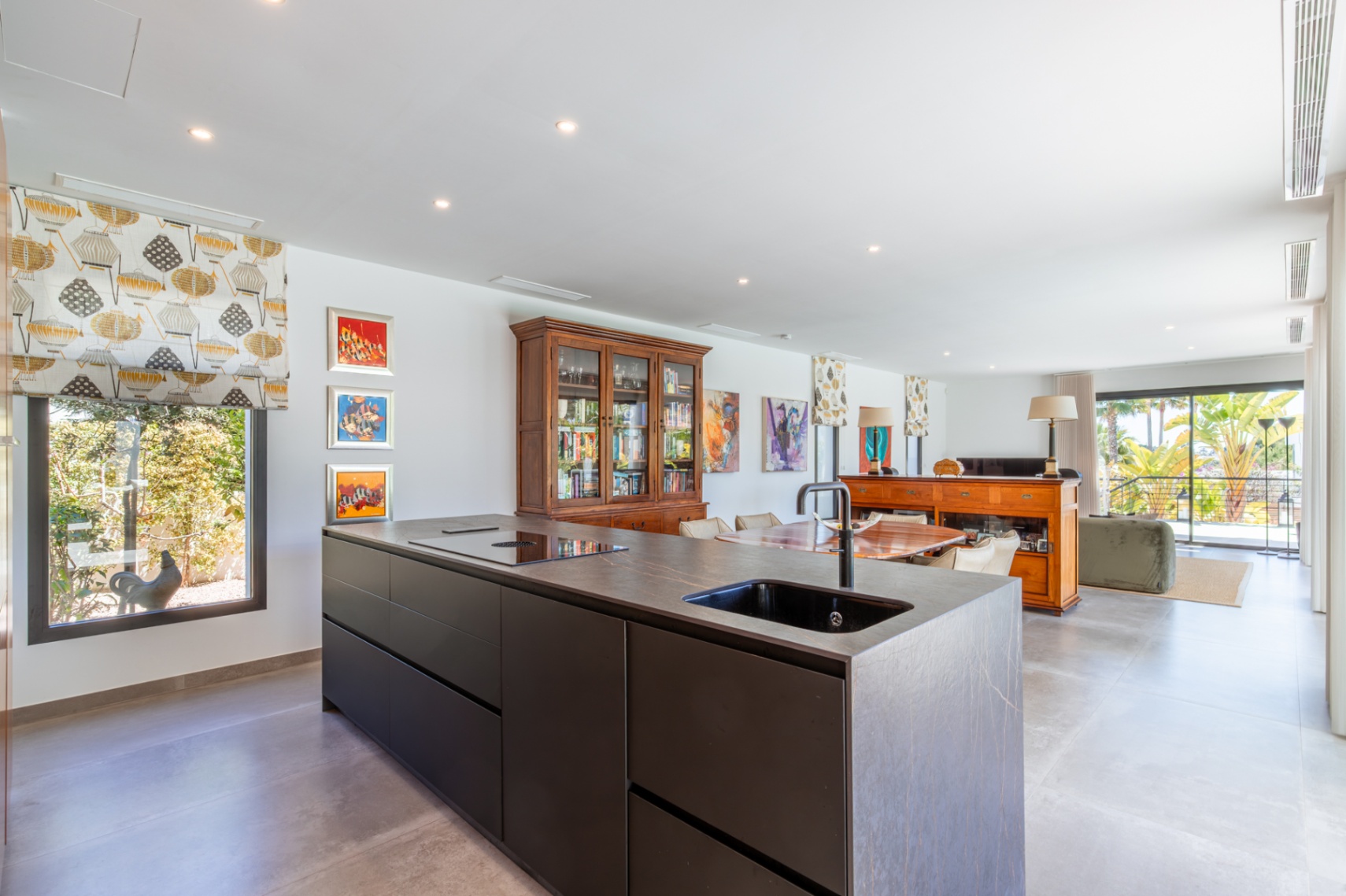 Cuisine moderne avec îlot en pierre sombre, évier intégré et plaque à induction, ouverte sur un séjour lumineux donnant accès à la terrasse.