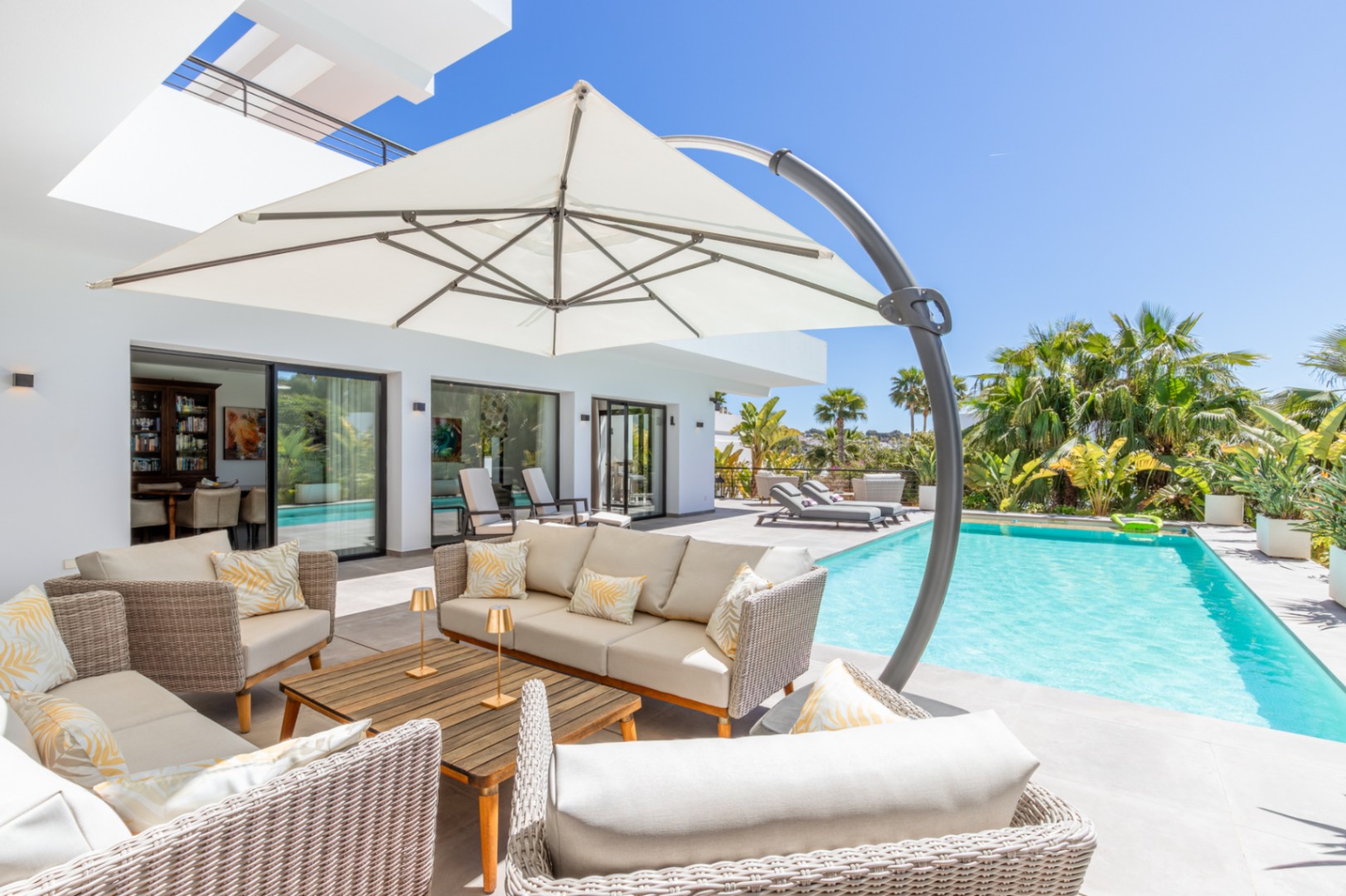 Espace détente extérieur avec mobilier en rotin et grand parasol près de la piscine, offrant un accès fluide au salon via des baies vitrées.