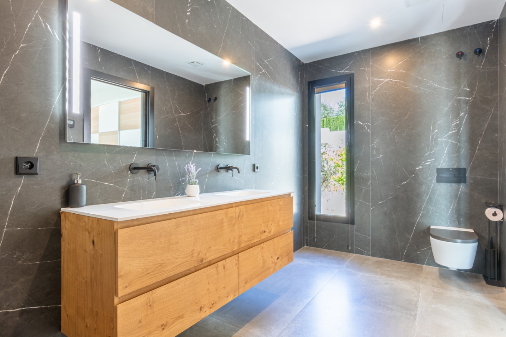 Salle de bain moderne avec carrelage effet marbre sombre, meuble double vasque en bois et robinetterie noire. Comprend un WC suspendu et un grand miroir avec éclairage LED intégré.