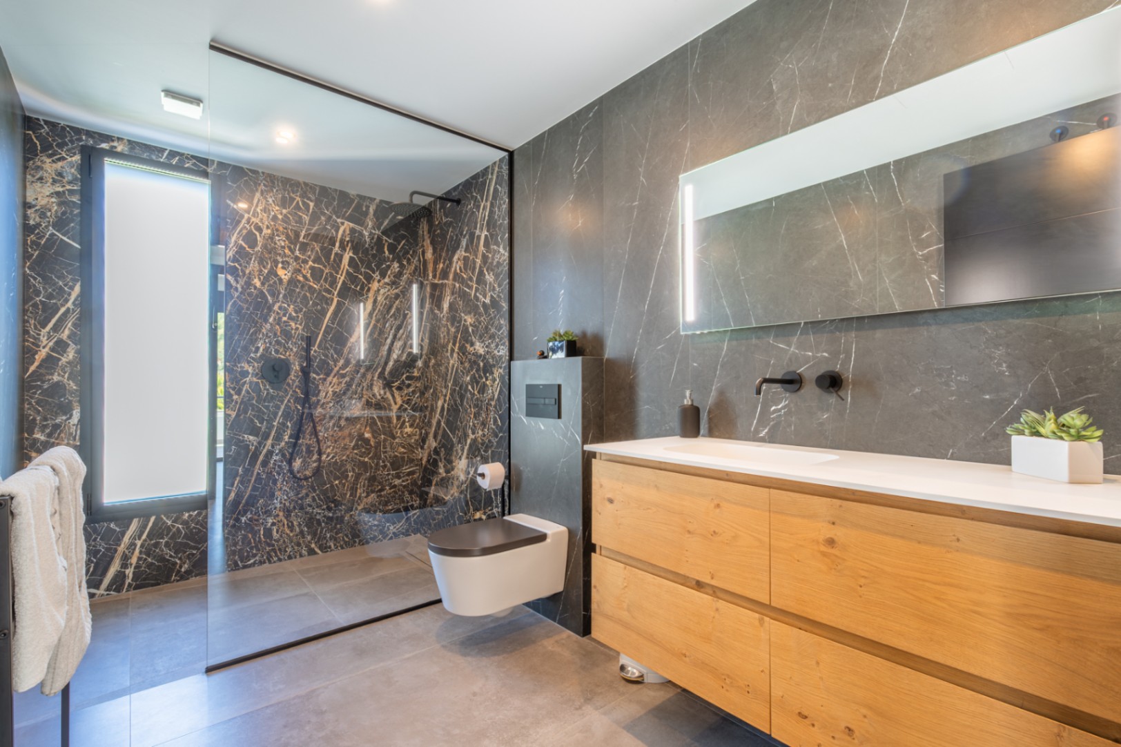 Salle de bain moderne avec carrelage effet marbre sombre, meuble sous-vasque en bois naturel et douche à l'italienne spacieuse avec paroi en verre.