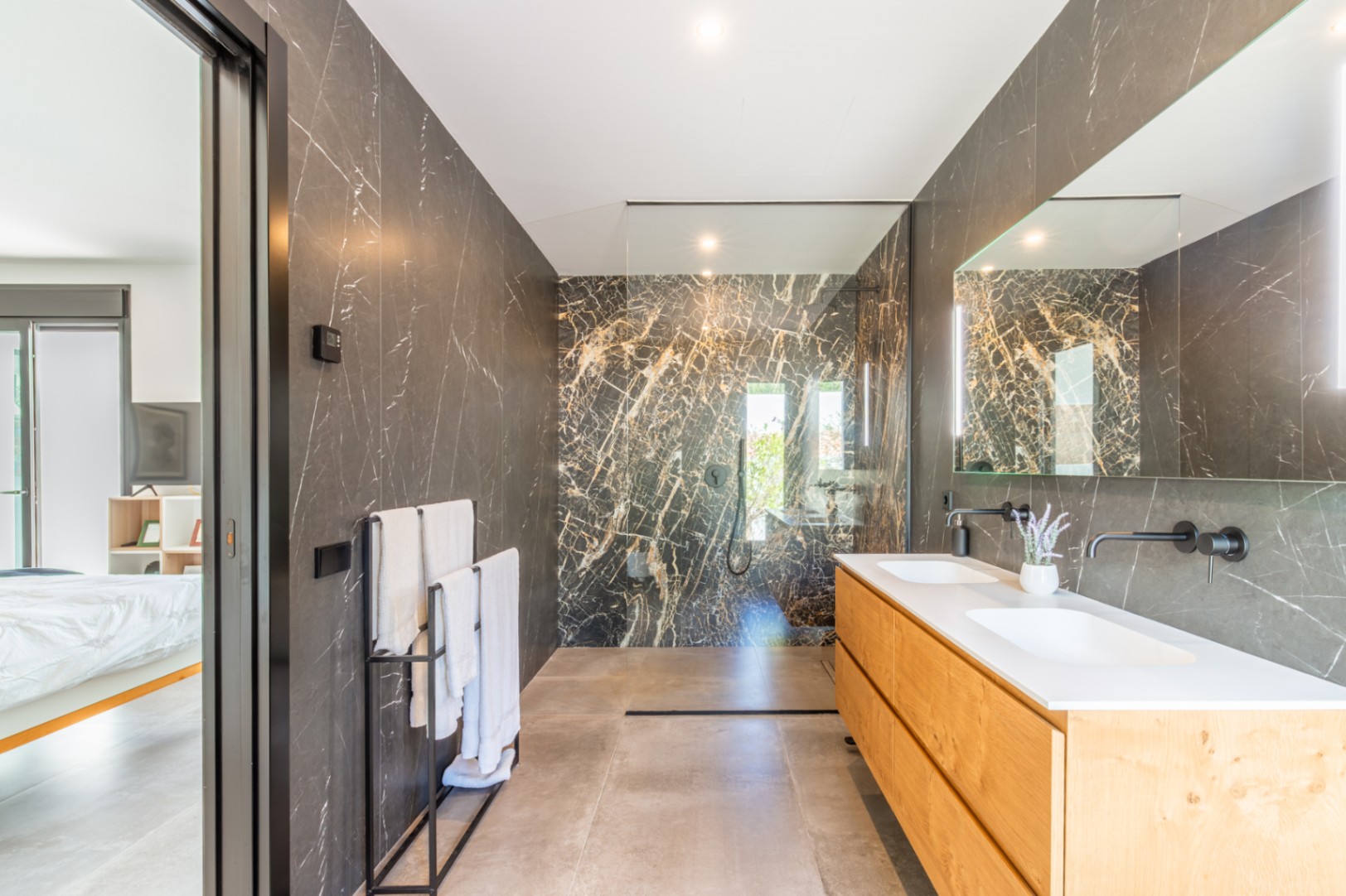 Salle de bain principale avec murs en marbre sombre, double vasque en bois et robinetterie noire encastrée, attenante à la chambre.