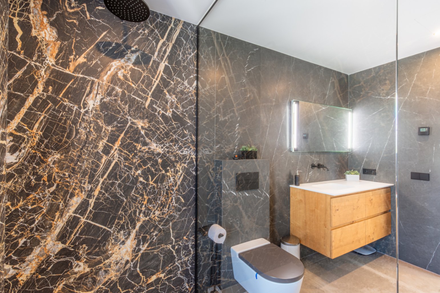 Salle de bains moderne avec douche à l'italienne, carrelage effet marbre noir, meuble vasque suspendu en bois et miroir rétroéclairé.