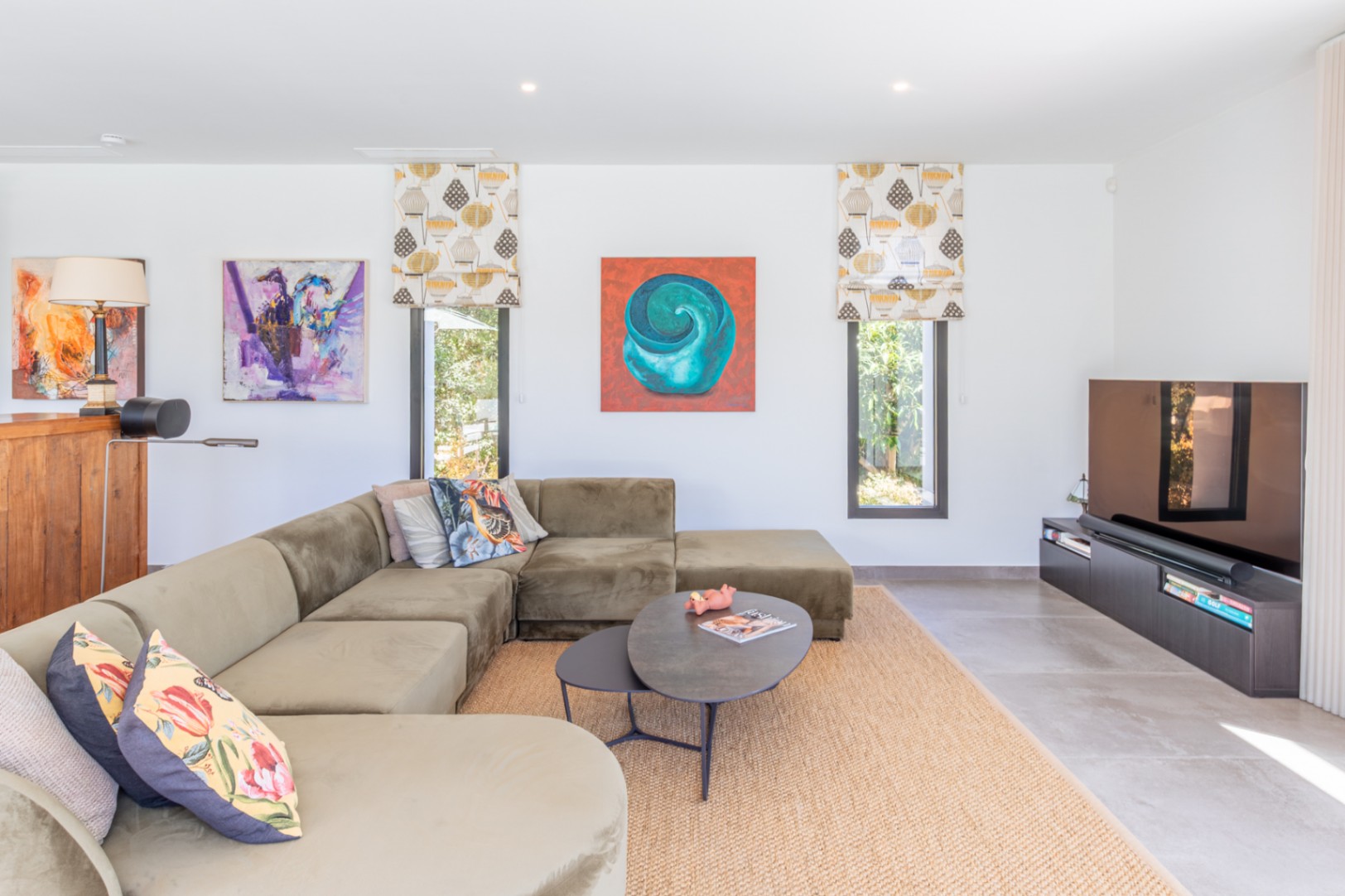 Salon contemporain avec un grand canapé d'angle vert olive, un tapis en jute et des fenêtres verticales apportant une lumière naturelle douce.