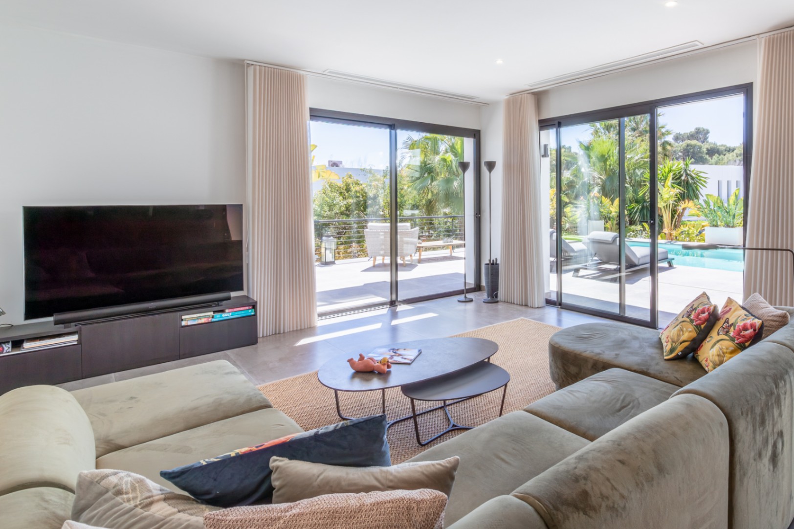 Salon lumineux avec canapé d'angle, grandes baies vitrées coulissantes offrant un accès direct à la terrasse avec piscine et au jardin méditerranéen.