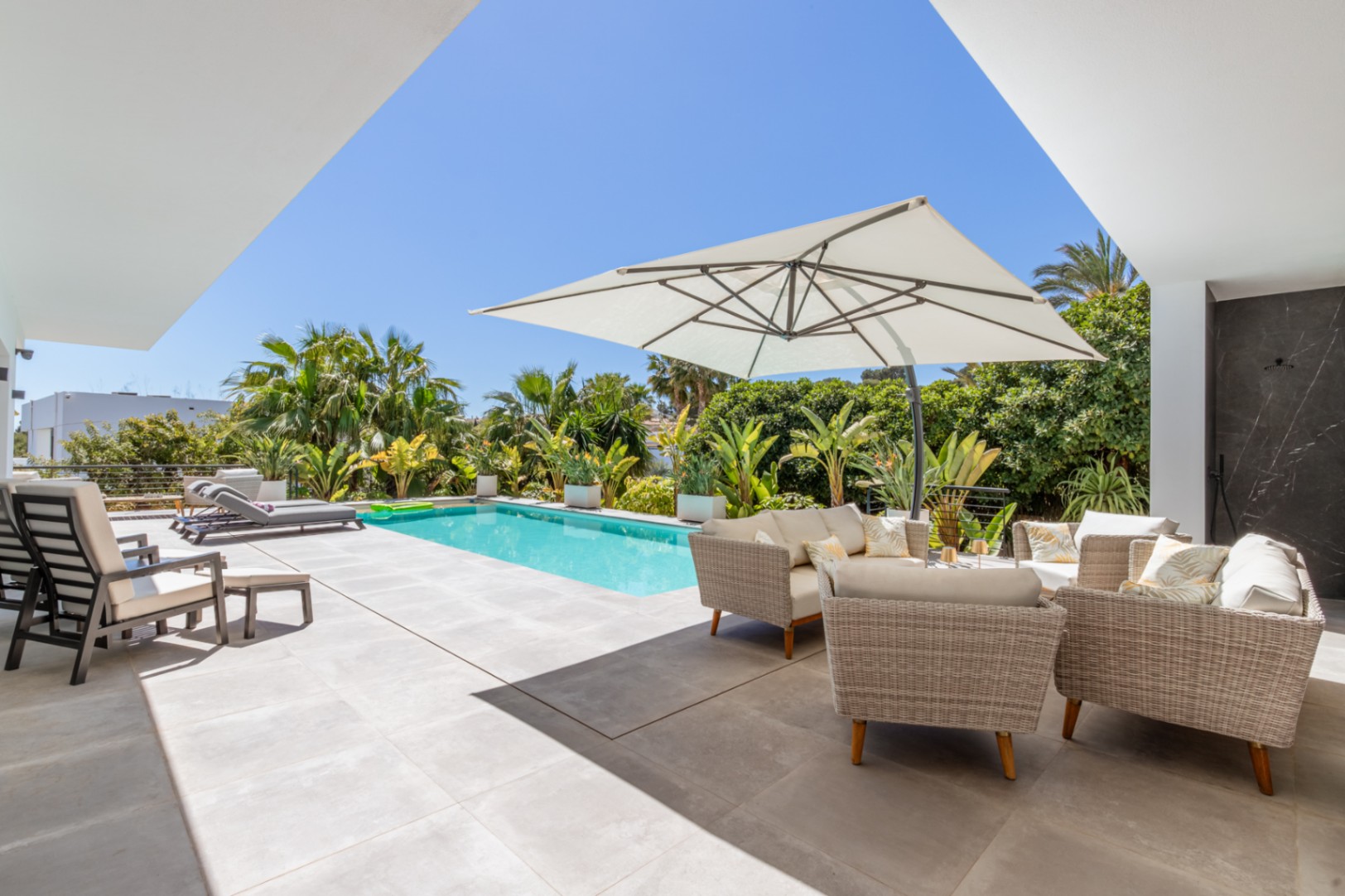 Terrasse extérieure avec piscine rectangulaire, salon de jardin en osier sous un grand parasol et végétation méditerranéenne offrant une intimité totale.