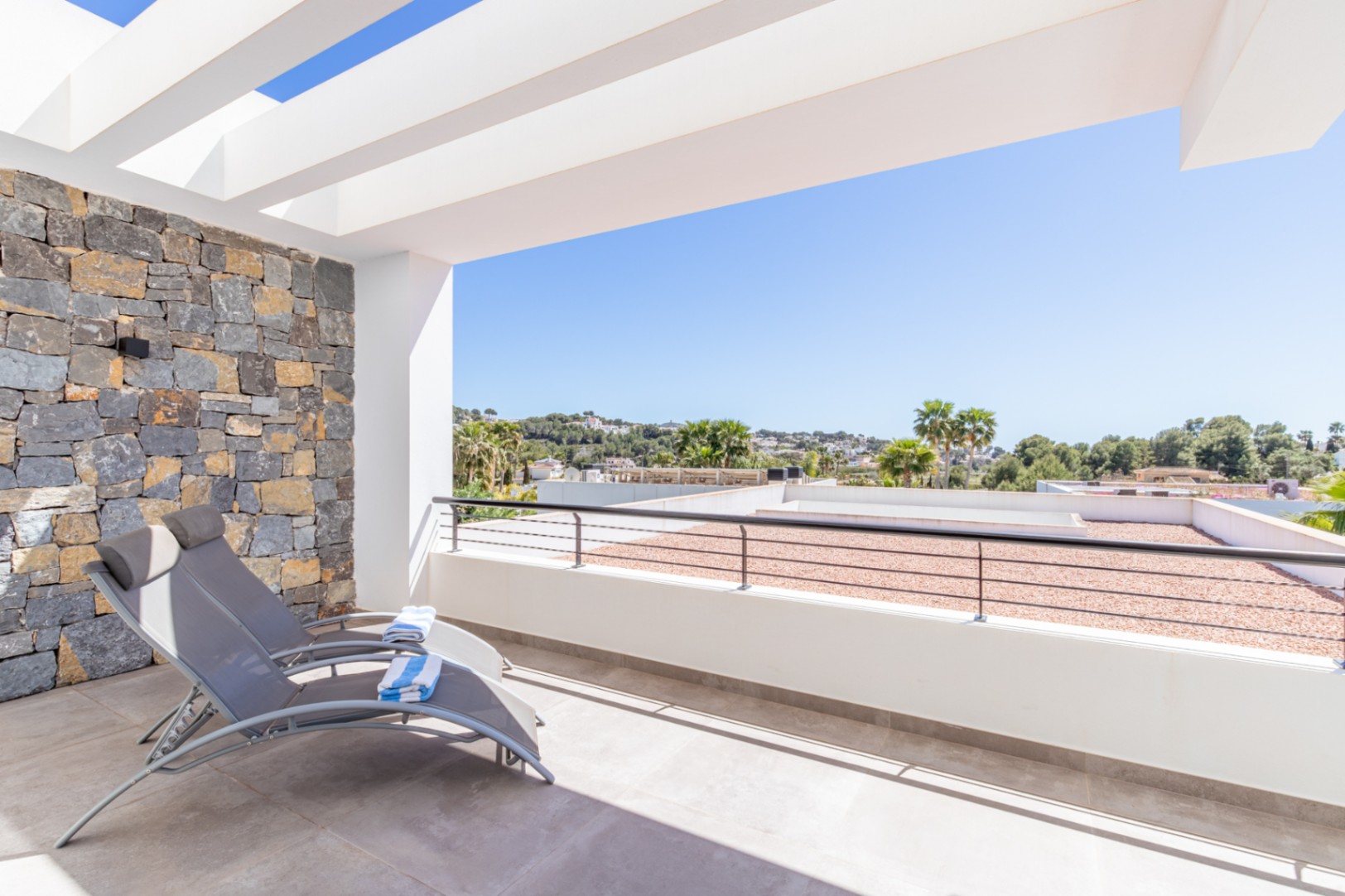 Terrasse privée à l'étage avec pergola blanche, mur en pierre naturelle et vue dégagée sur les environs de Moraira.