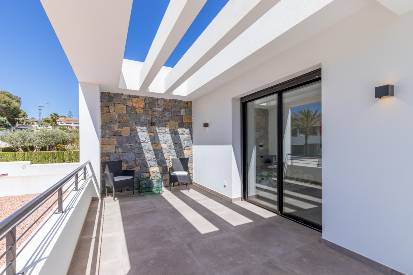 Terrasse privée avec pergola à poutres blanches, mur en pierre naturelle et grandes baies vitrées coulissantes offrant une luminosité optimale.