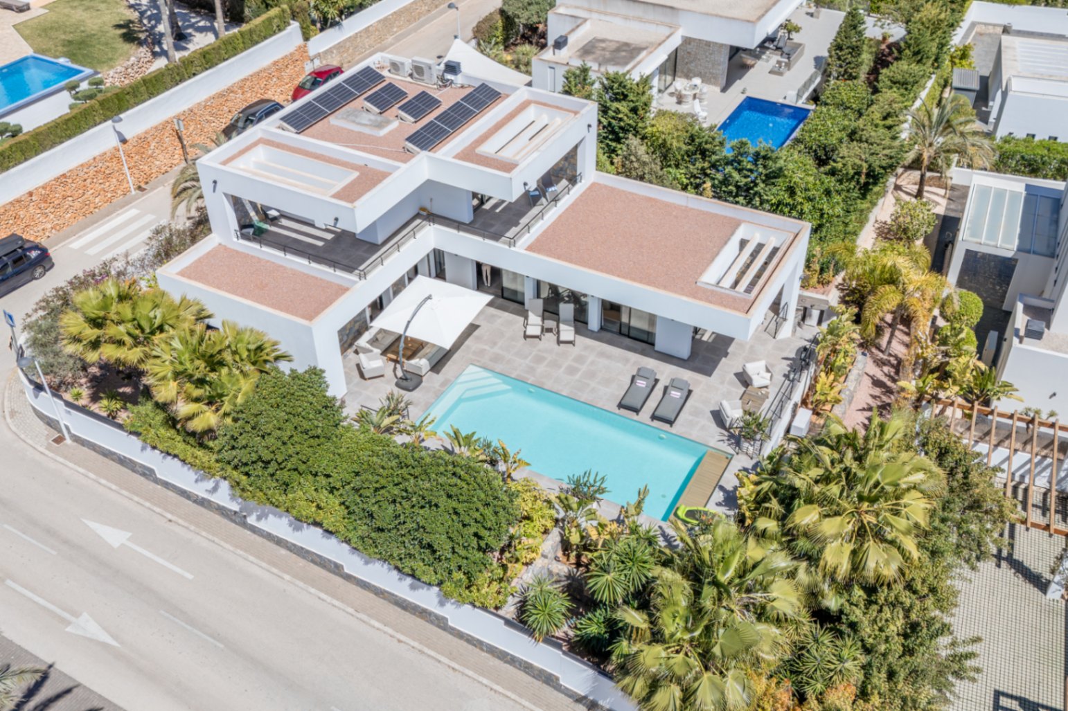 Vue aérienne de la villa moderne avec panneaux solaires, piscine rectangulaire et vastes terrasses entourées d'une végétation méditerranéenne dense.