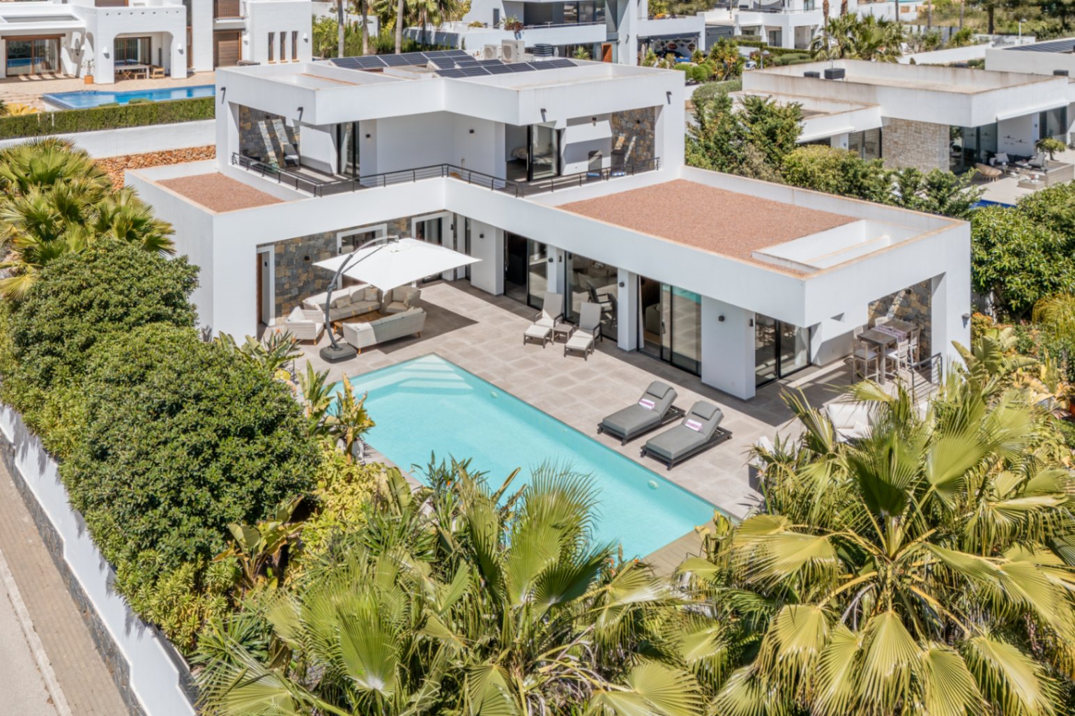 Vue aérienne de la villa moderne avec piscine, panneaux solaires en toiture et terrasses spacieuses entourées d'une végétation méditerranéenne.