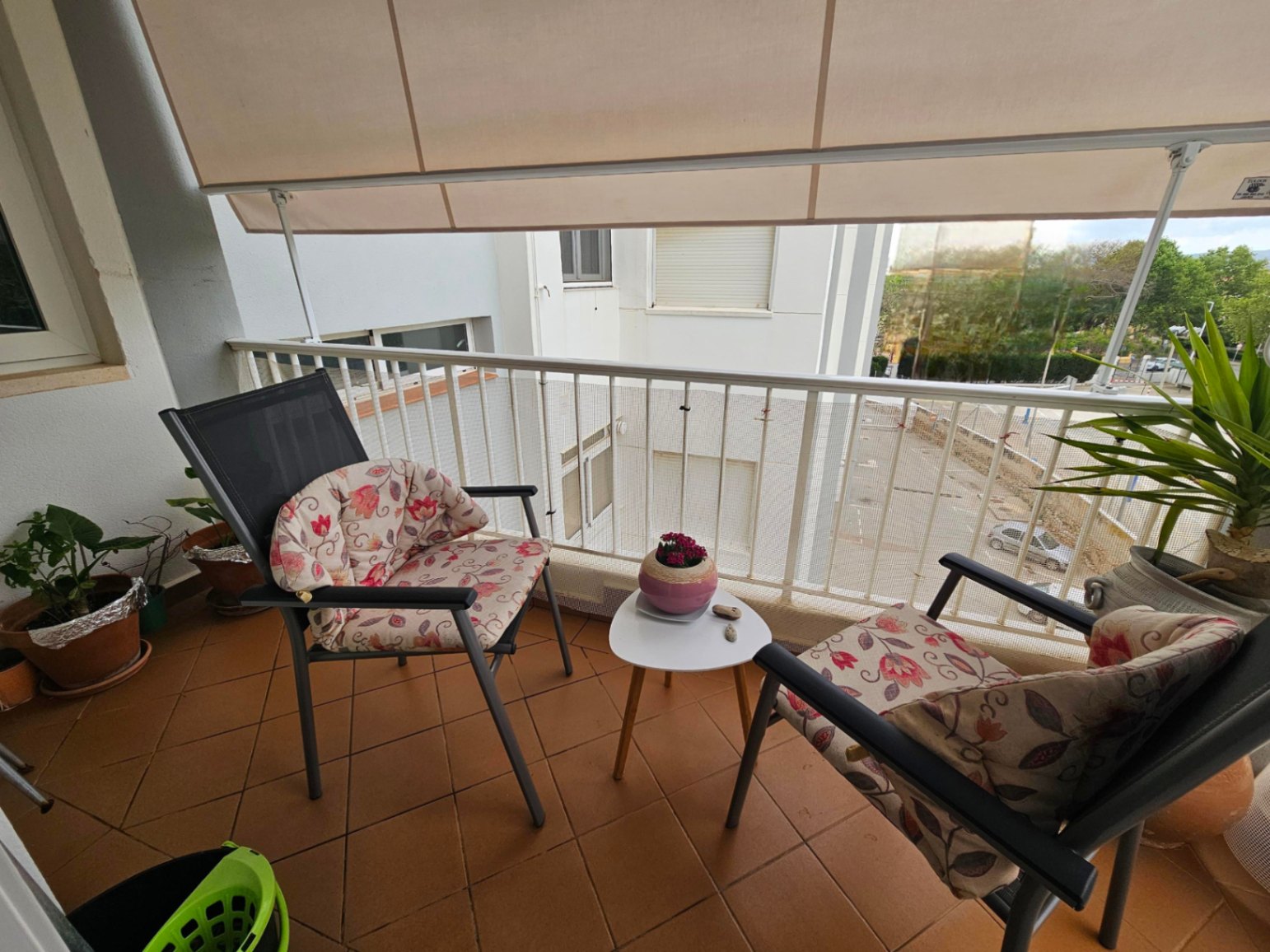 Balcon avec revêtement en terre cuite, équipé d'un store banne rétractable et d'un mobilier d'extérieur comprenant deux chaises et une petite table.