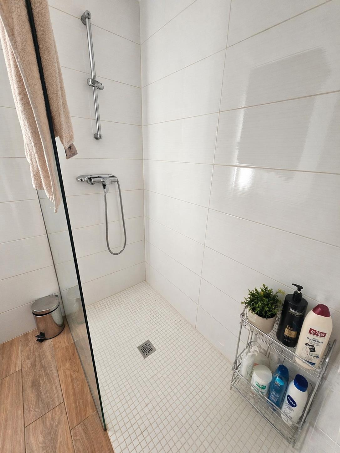 Douche à l'italienne avec sol en mosaïque blanche, paroi en verre et robinetterie chromée sur fond de carrelage mural horizontal.