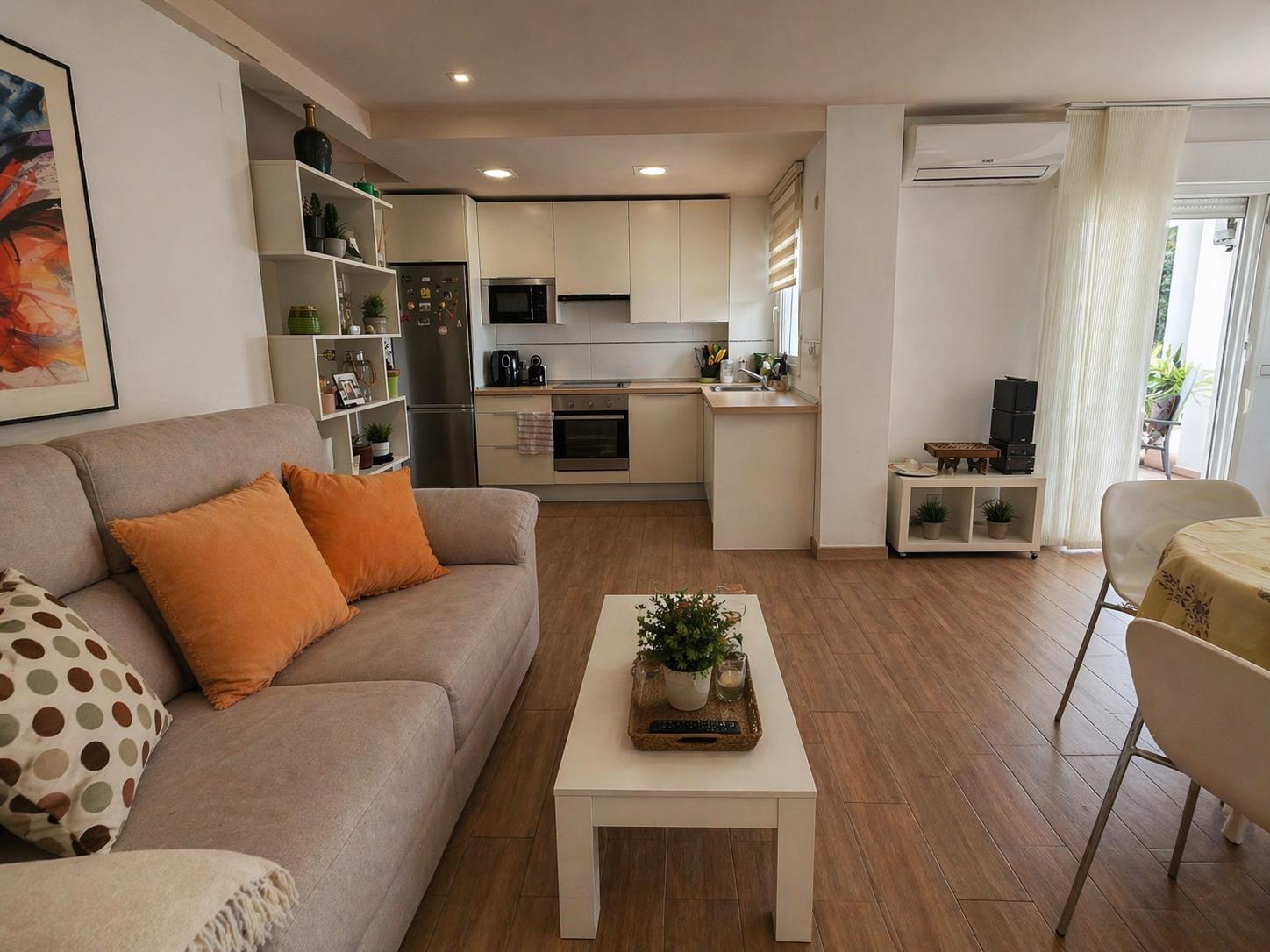 Espace de vie ouvert avec sol en grès imitation bois, cuisine moderne équipée et accès à la terrasse, le tout éclairé par des spots encastrés au plafond.