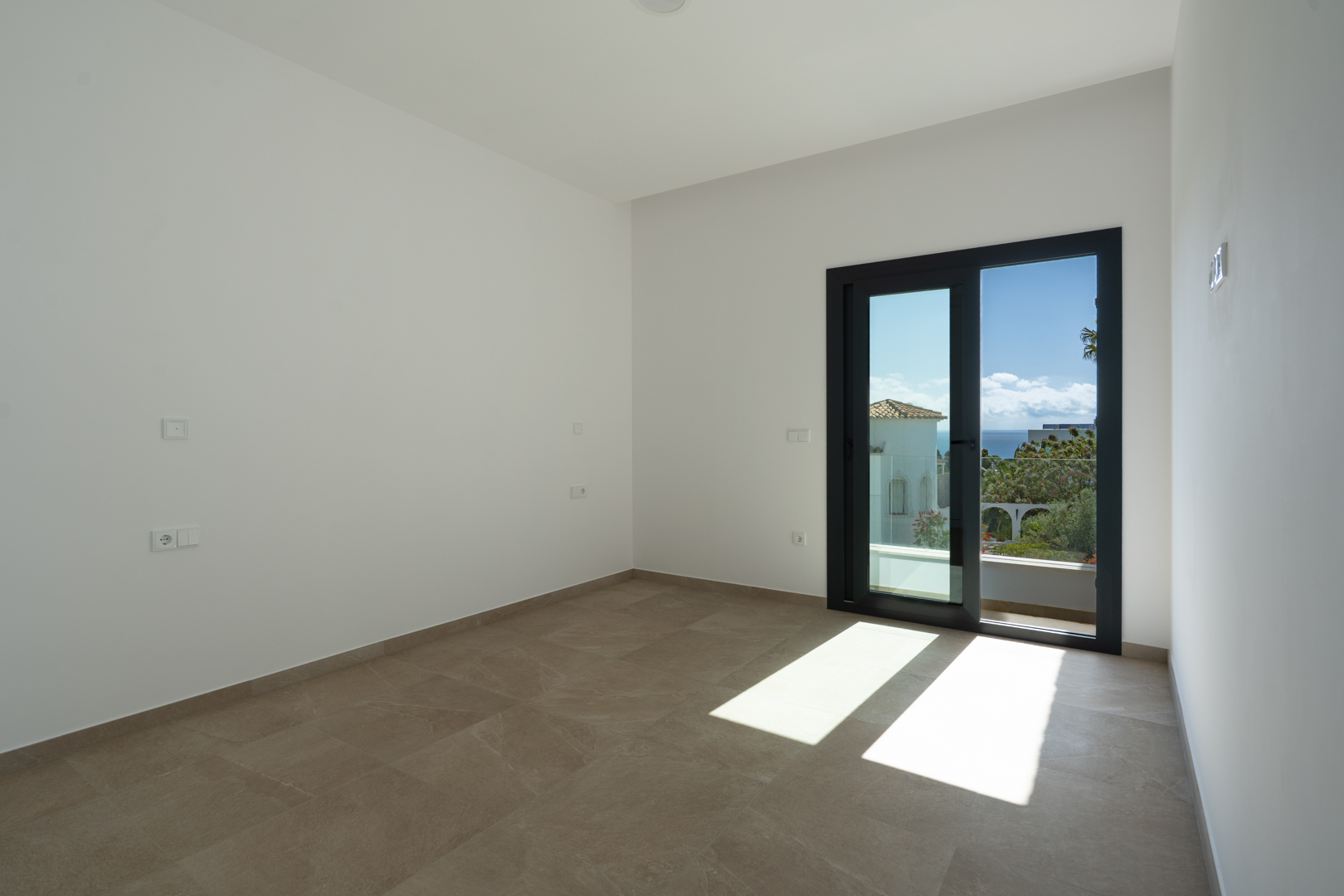 Chambre lumineuse avec carrelage en grès cérame et accès direct à une terrasse privée offrant une vue dégagée sur la mer Méditerranée.