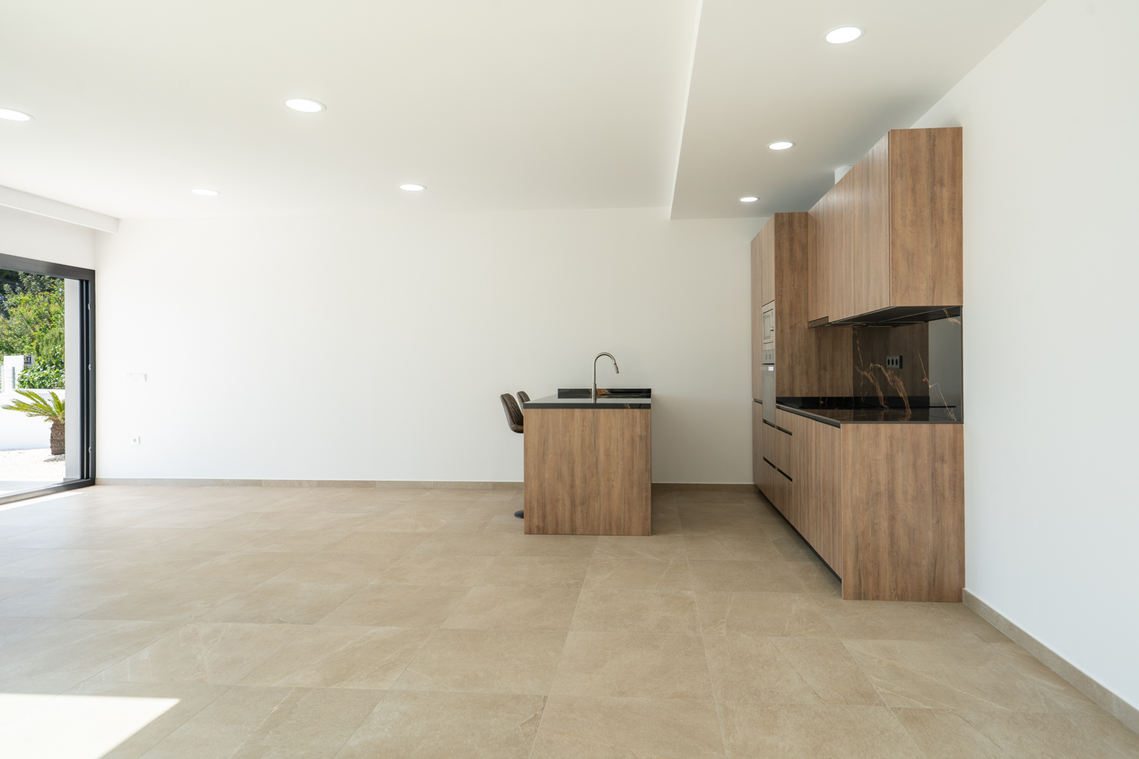 Cuisine design avec meubles en bois, plan de travail sombre veiné et îlot central, intégrée dans un espace ouvert avec sol en grès cérame et éclairage encastré.