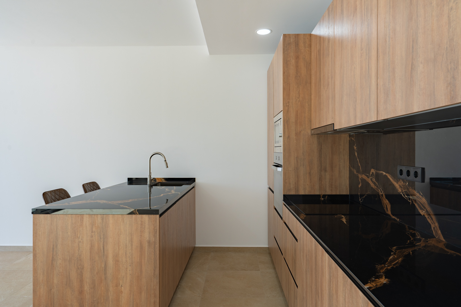 Cuisine design avec meubles finition bois, plans de travail en pierre sombre veinée et îlot central avec évier intégré et robinetterie minimaliste.