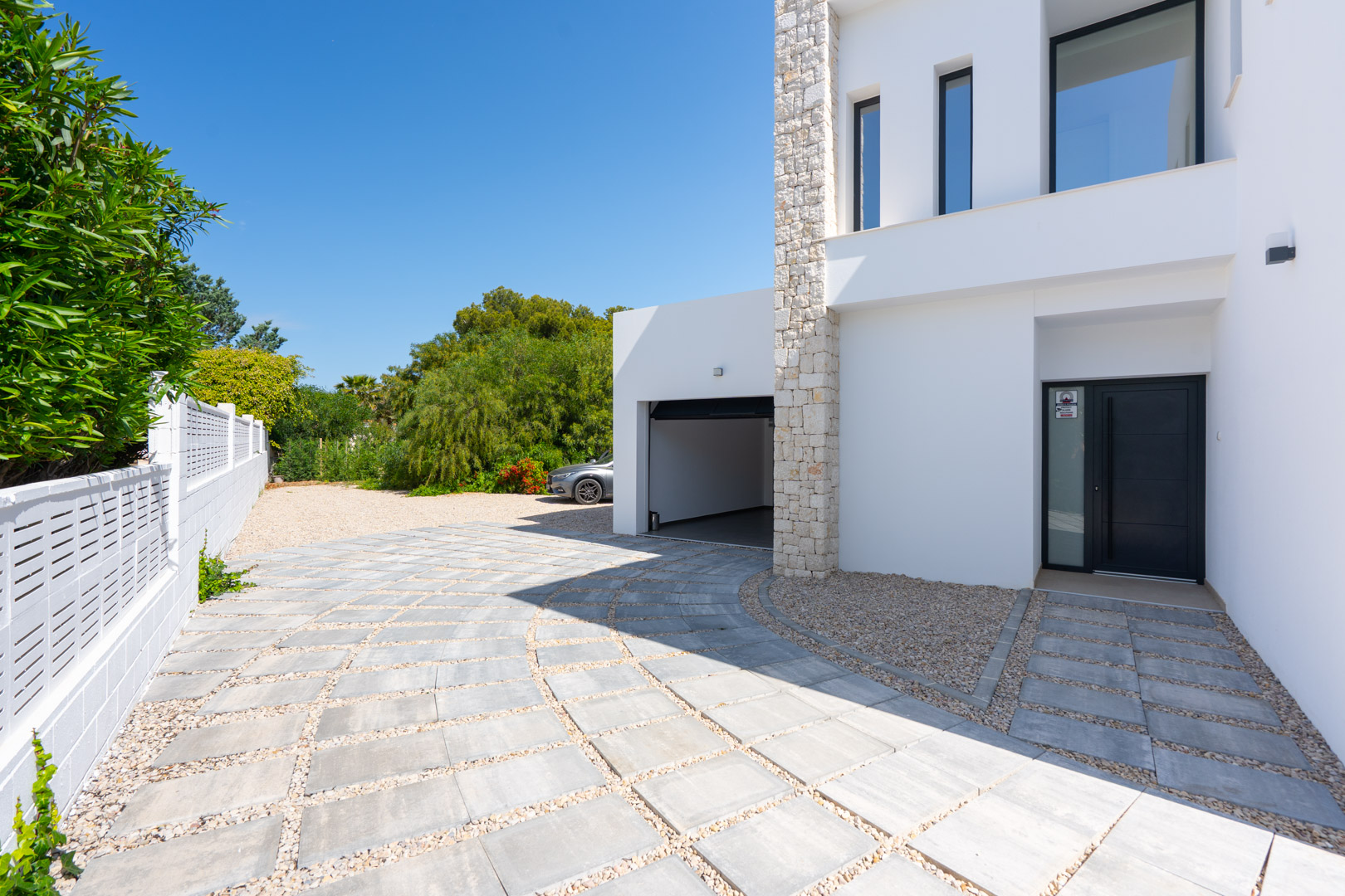 Entrée principale et accès au garage avec une allée pavée et gravillonnée, mettant en valeur la façade blanche et un mur en pierre naturelle.