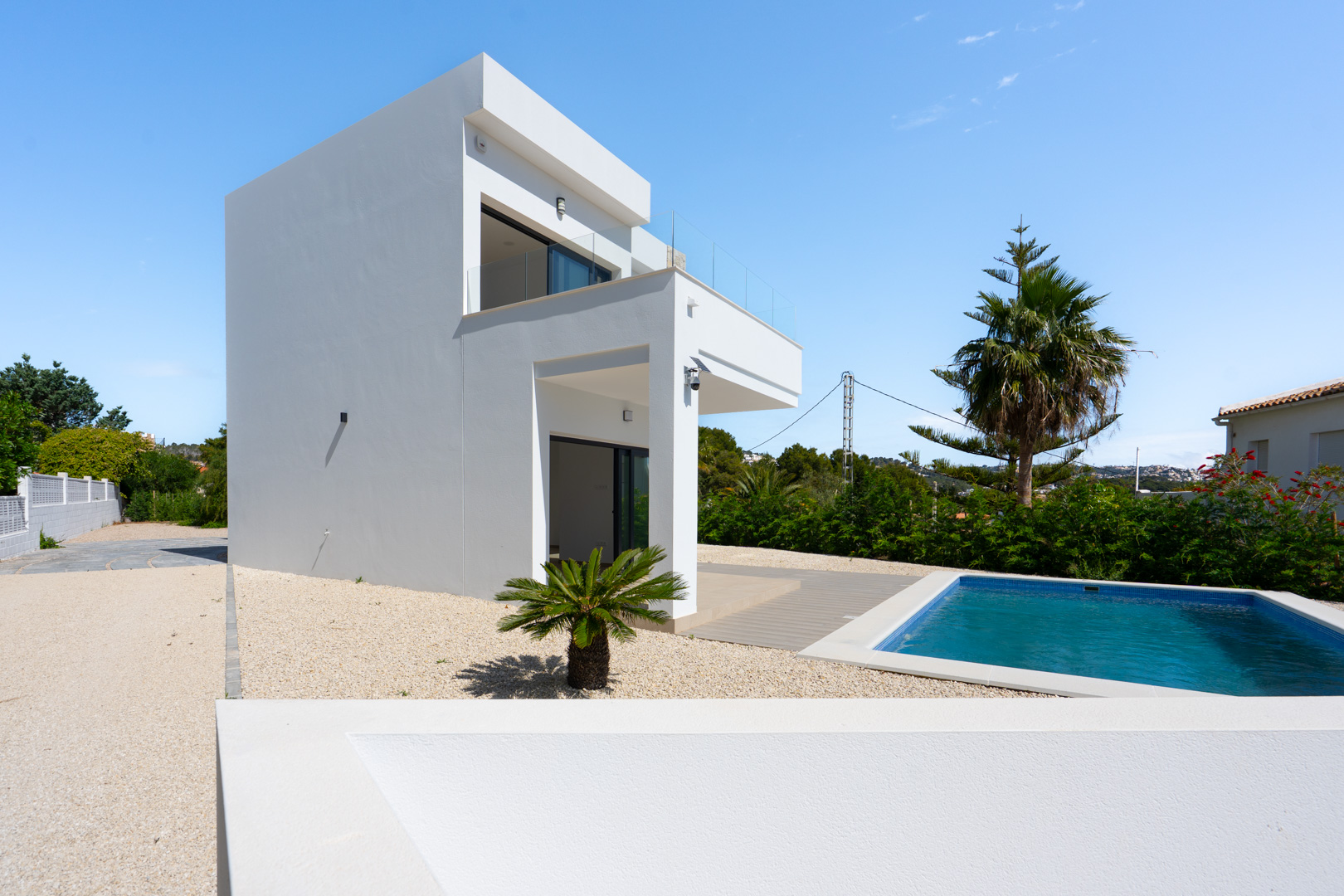 Extérieur de la villa moderne aux lignes épurées, comprenant une piscine rectangulaire, un jardin en gravier et des terrasses avec garde-corps en verre.