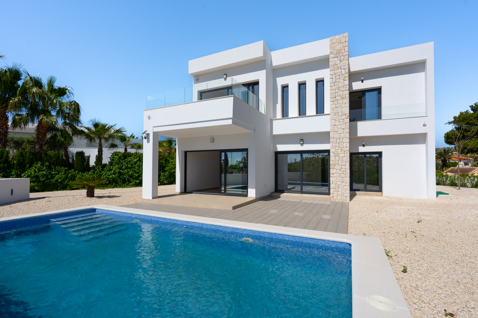 Façade moderne à deux niveaux avec mur en pierre naturelle, piscine rectangulaire et terrasses avec garde-corps en verre au cœur d'un jardin méditerranéen.