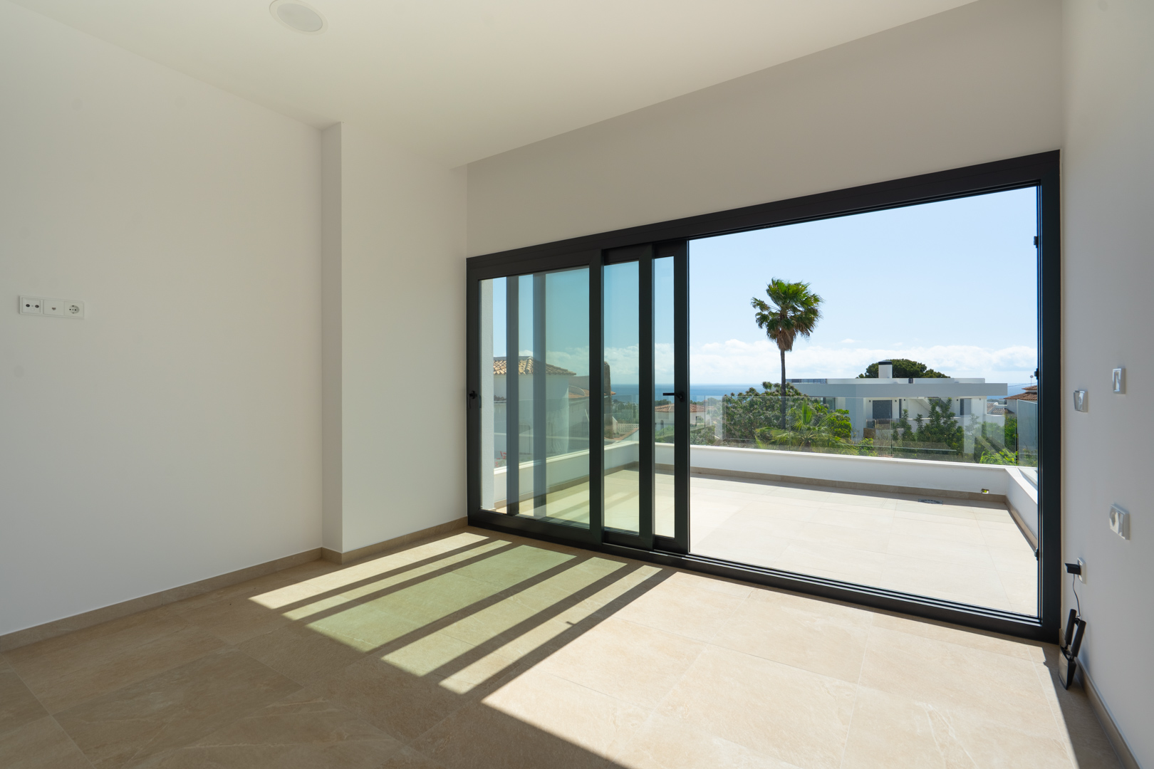 Intérieur lumineux avec sol en grès cérame et grandes baies vitrées coulissantes ouvrant sur une terrasse privée avec vue sur la mer Méditerranée.