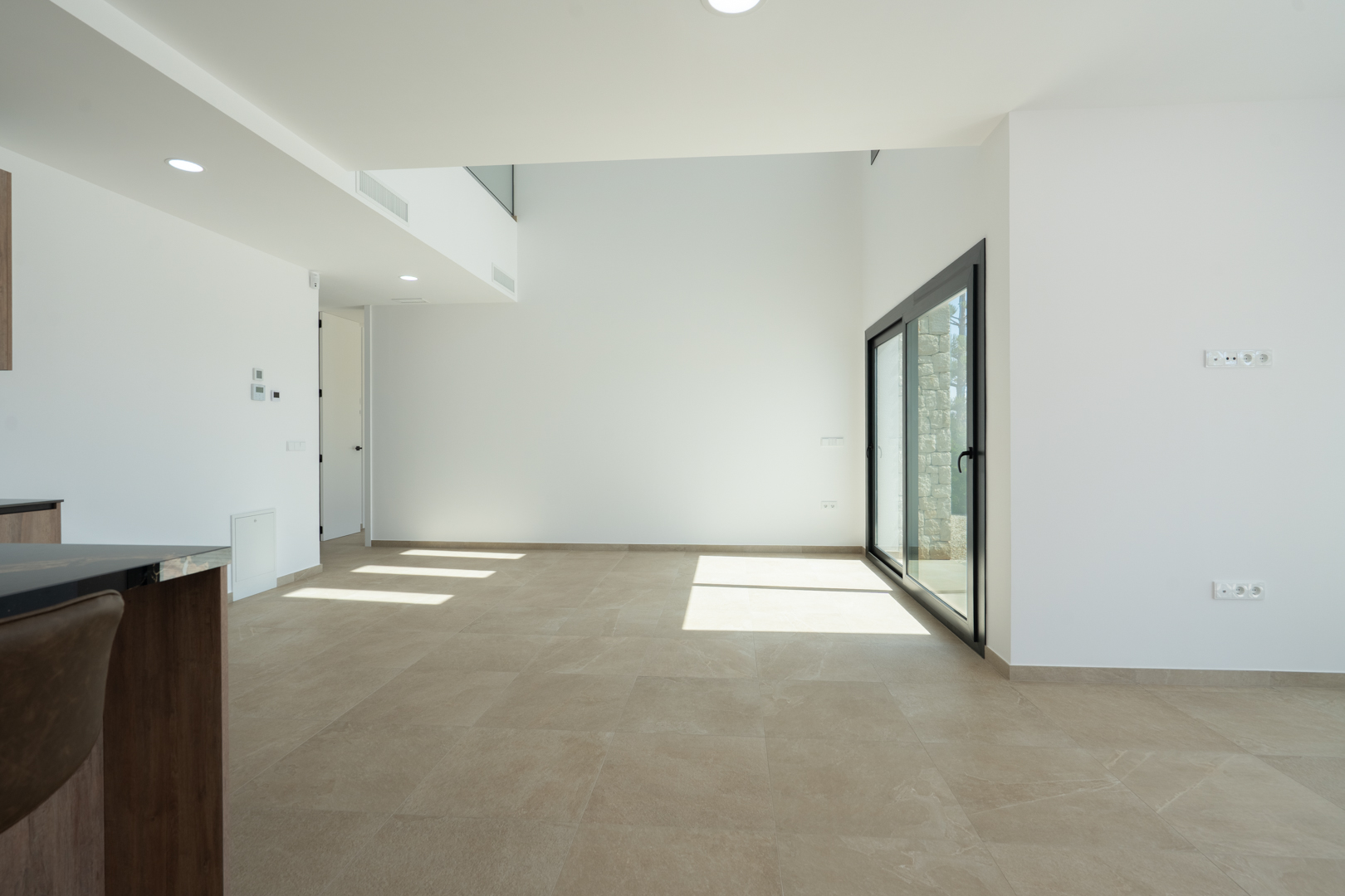 Salon-salle à manger à aire ouverte avec plafonds à double hauteur, sol en grès cérame grand format et larges baies vitrées offrant une luminosité naturelle.