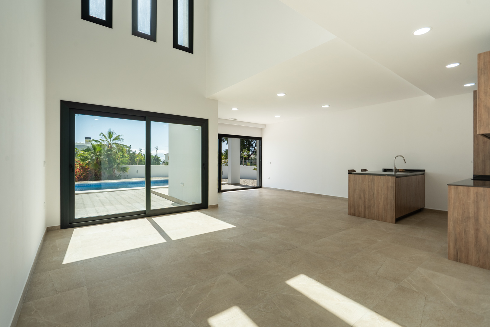 Séjour spacieux à double hauteur avec cuisine ouverte, carrelage en grès cérame et larges baies vitrées offrant un accès direct à la piscine.