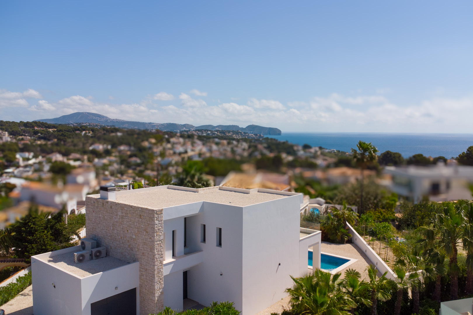 Vue aérienne de la villa moderne aux façades blanches et accents en pierre naturelle, avec piscine privée et vue panoramique sur la mer Méditerranée.