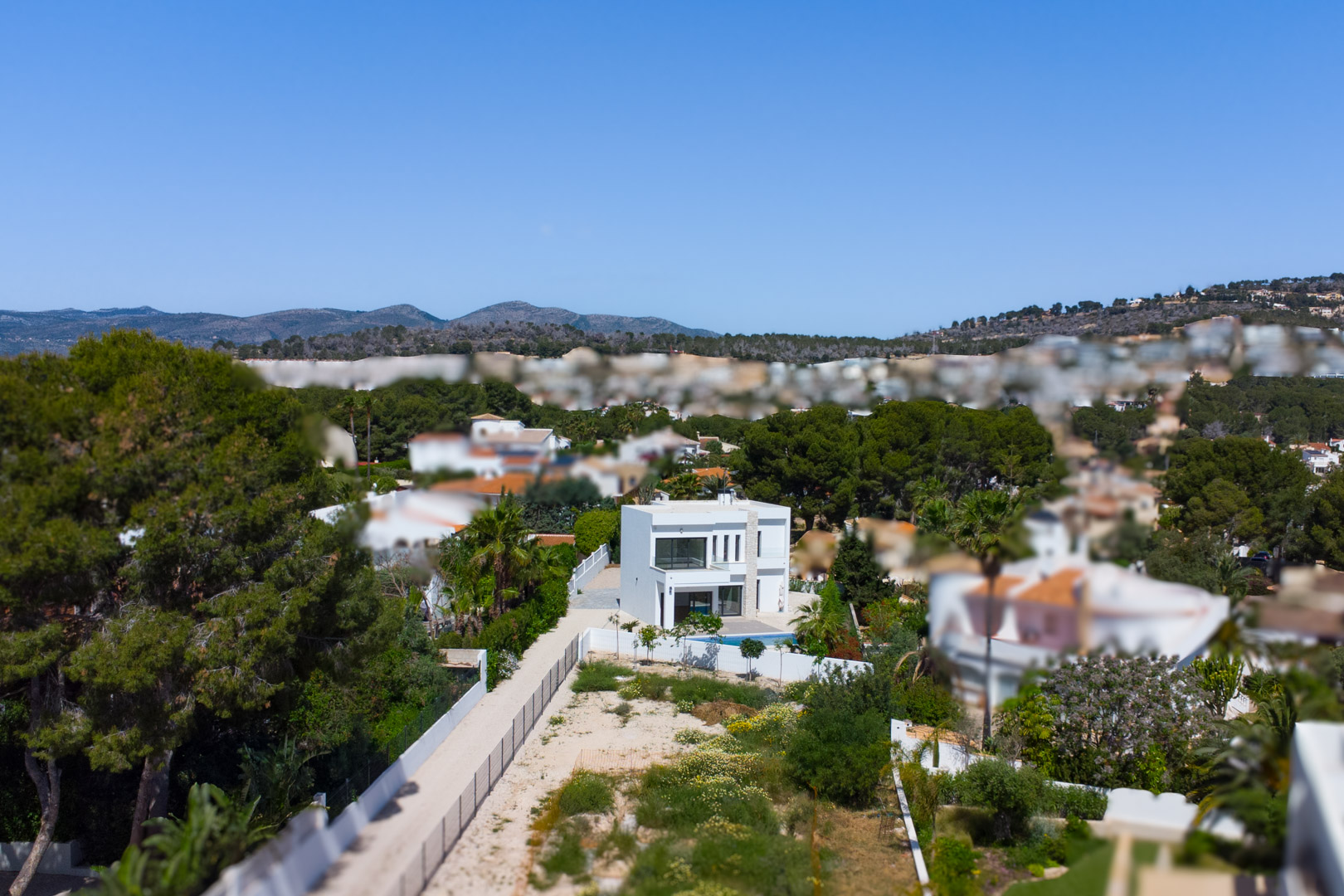 Vue aérienne de la villa moderne située sur un vaste terrain plat, entourée d'une pinède méditerranéenne avec les montagnes en arrière-plan.