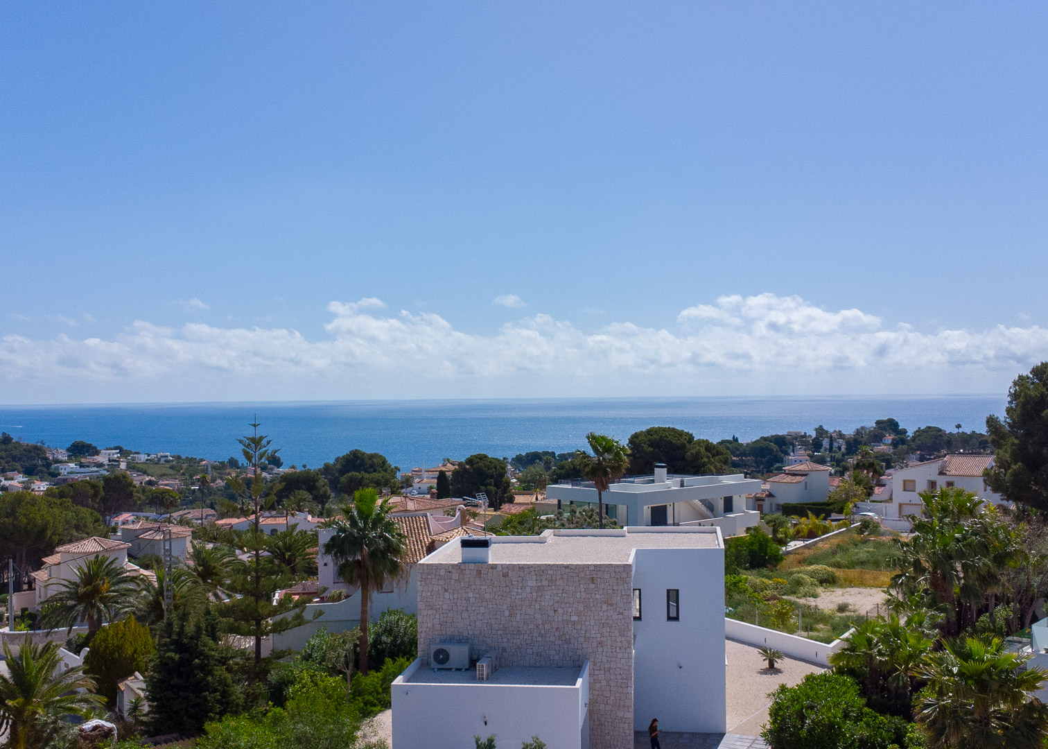 Vue surélevée de l'architecture moderne avec des accents en pierre naturelle, offrant une vue panoramique sur la mer Méditerranée et la verdure de Benissa.