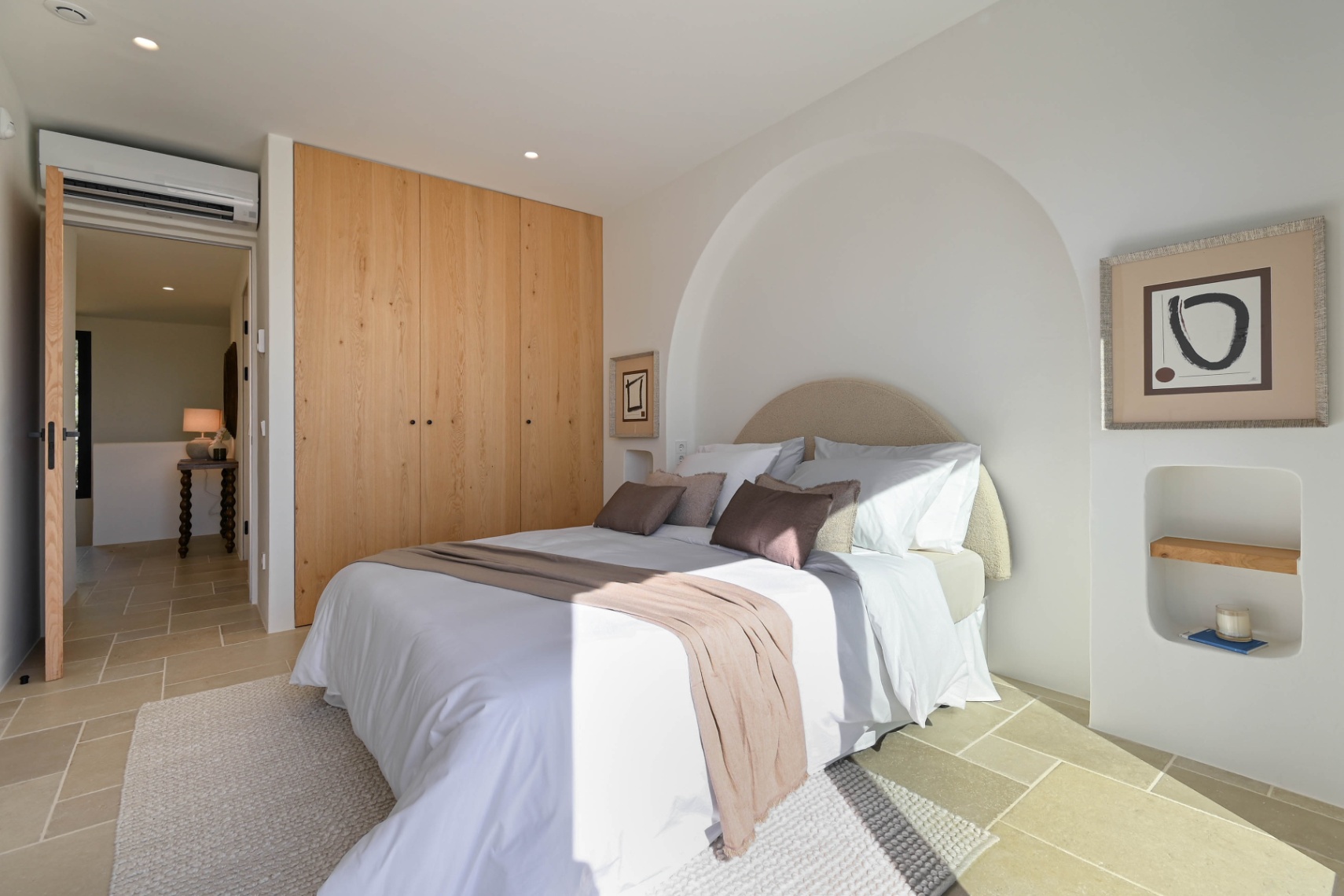 Chambre élégante avec placards en bois, sol en pierre naturelle et une niche murale en arche. Équipée de la climatisation et d'un éclairage encastré minimaliste.