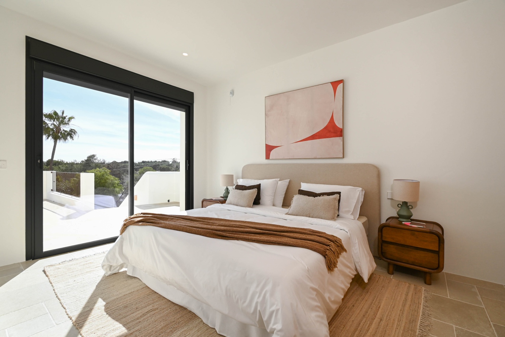 Chambre lumineuse avec de grandes baies vitrées noires, accès direct à la terrasse et sol en pierre naturelle aux tons neutres.