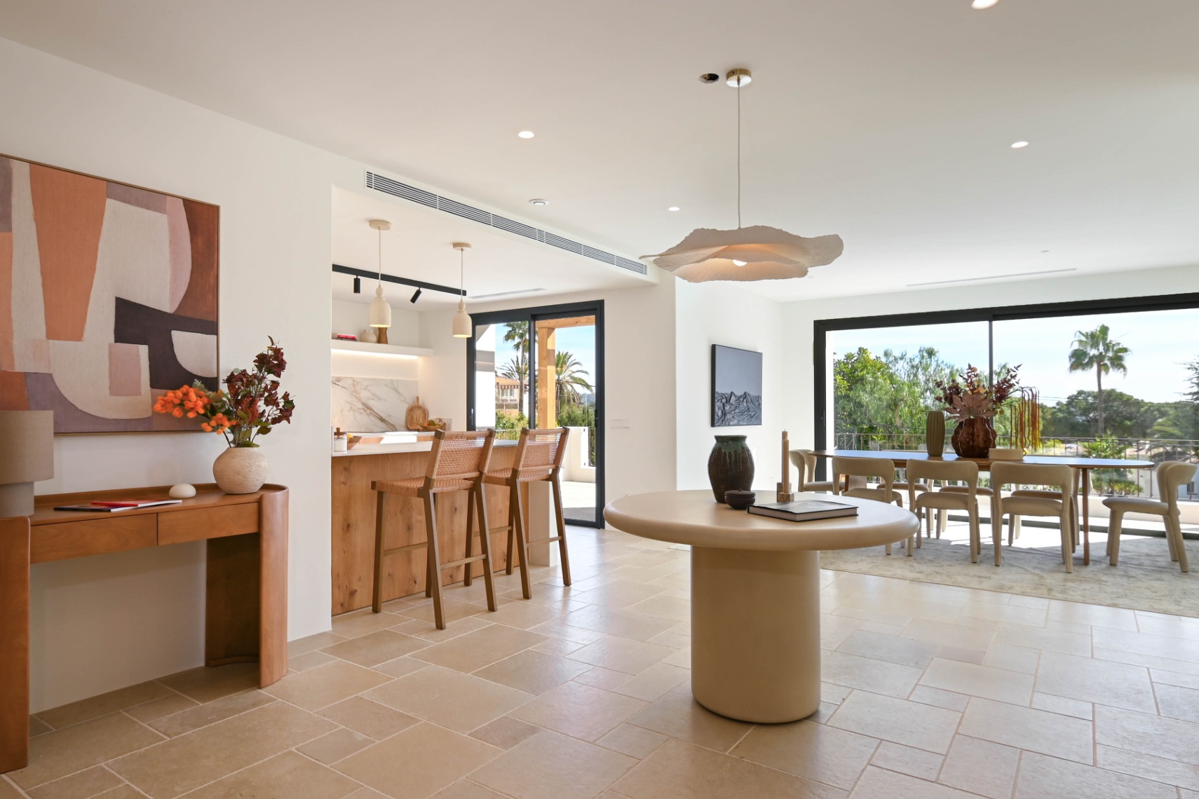 Espace de vie à aire ouverte avec sol en pierre naturelle, cuisine intégrée avec îlot en bois et salle à manger lumineuse ouvrant sur la terrasse par de larges baies vitrées.