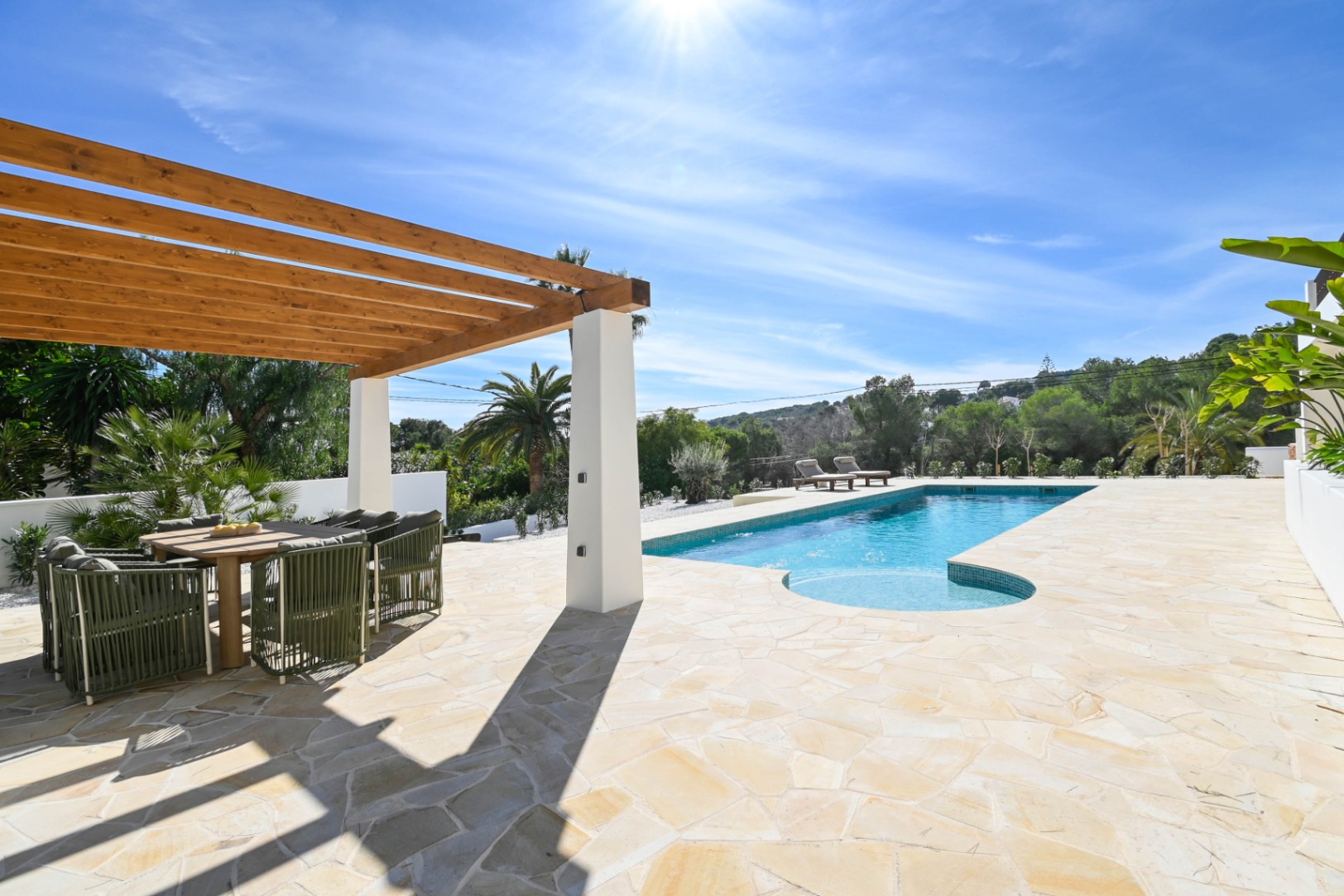 Terrasse extérieure avec dallage en pierre naturelle, pergola en bois abritant un coin repas et piscine de 13 mètres entourée de jardins méditerranéens.