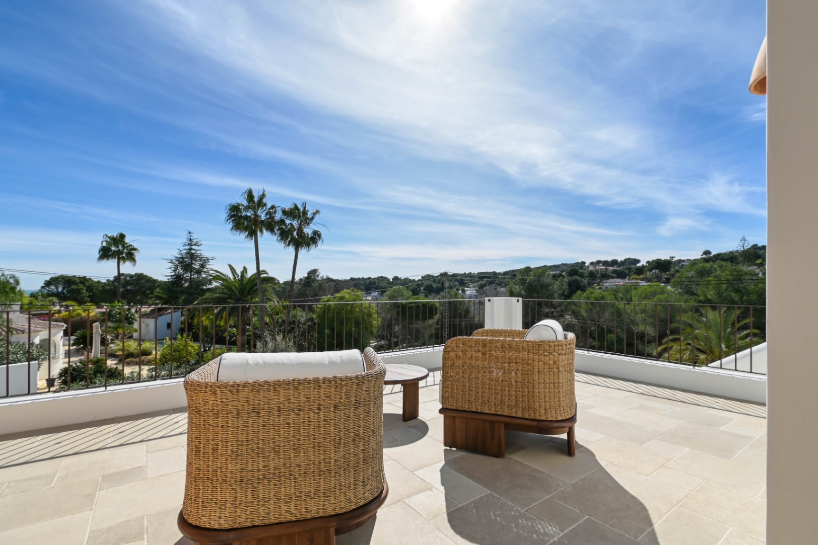 Terrasse supérieure avec revêtement en pierre naturelle et fauteuils en osier, offrant une vue panoramique sur la végétation environnante.