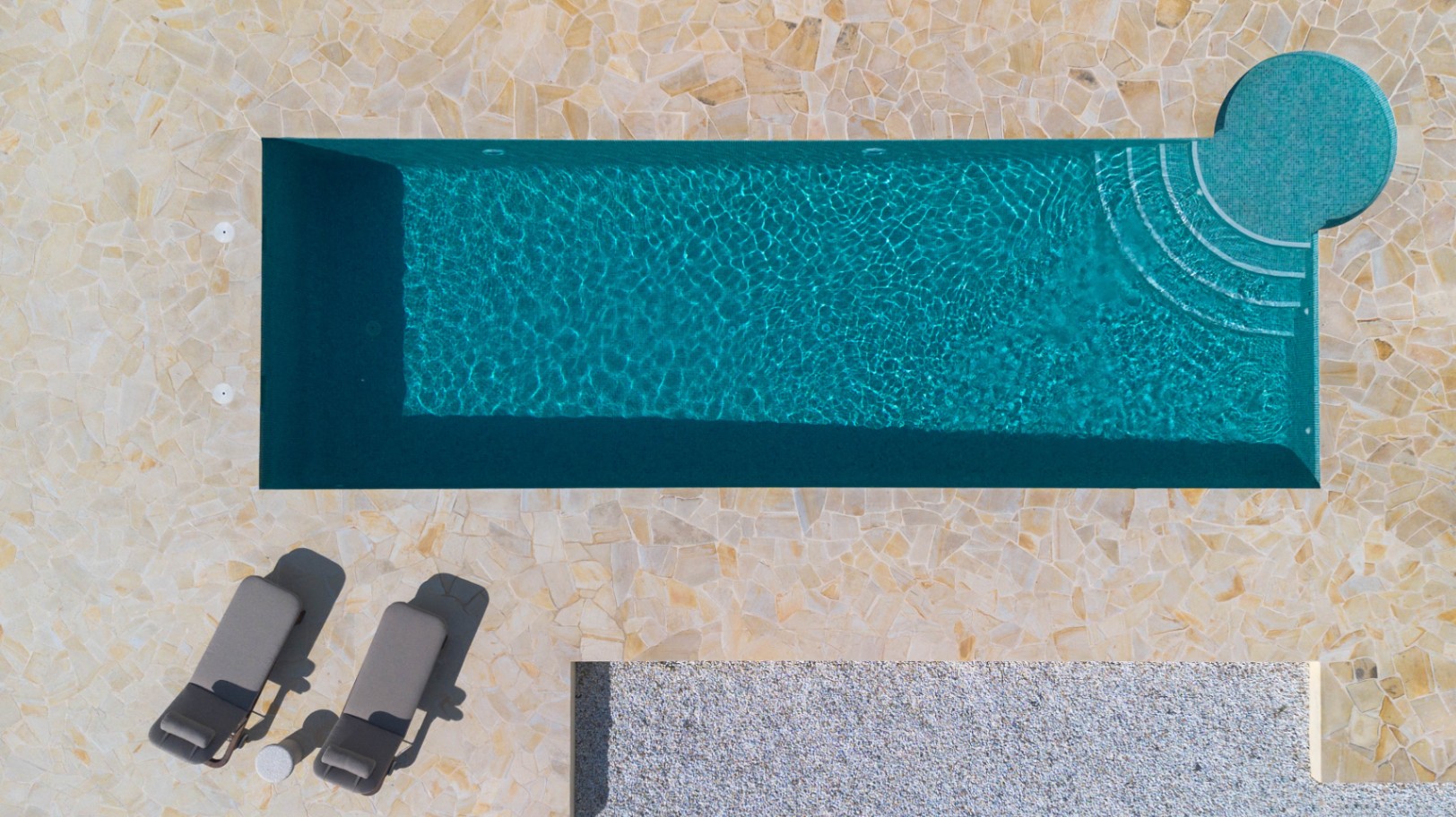 Vue aérienne de la piscine de 13 mètres avec mosaïque turquoise, escalier circulaire intégré et terrasse en dalles de pierre naturelle irrégulières.