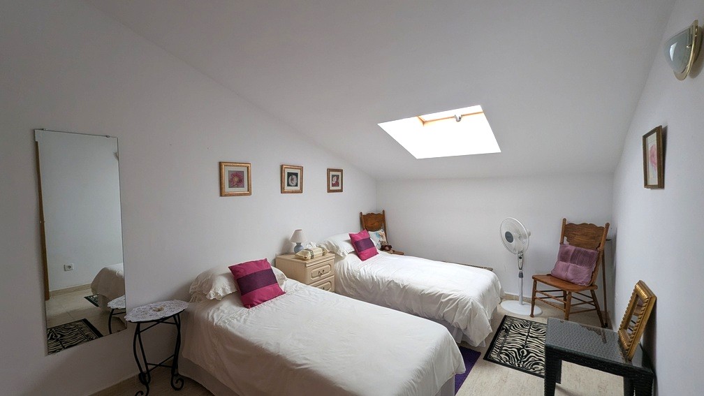 Chambre mansardée avec deux lits simples, un puits de lumière naturel et un sol en carrelage clair.